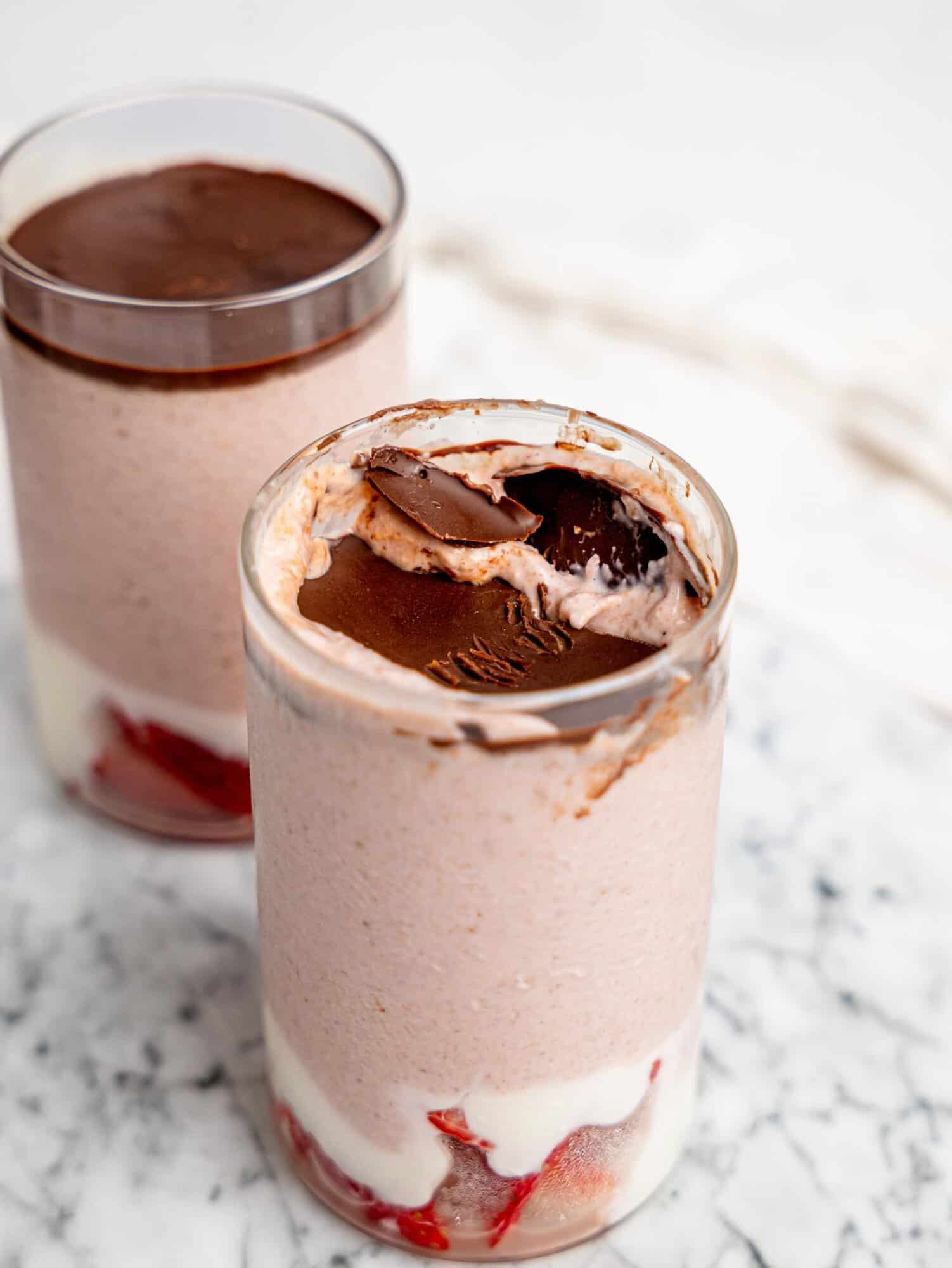 Close-up of strawberry blended overnight oats topped with a set chocolate layer that has been cracked, revealing the creamy oat mixture underneath.