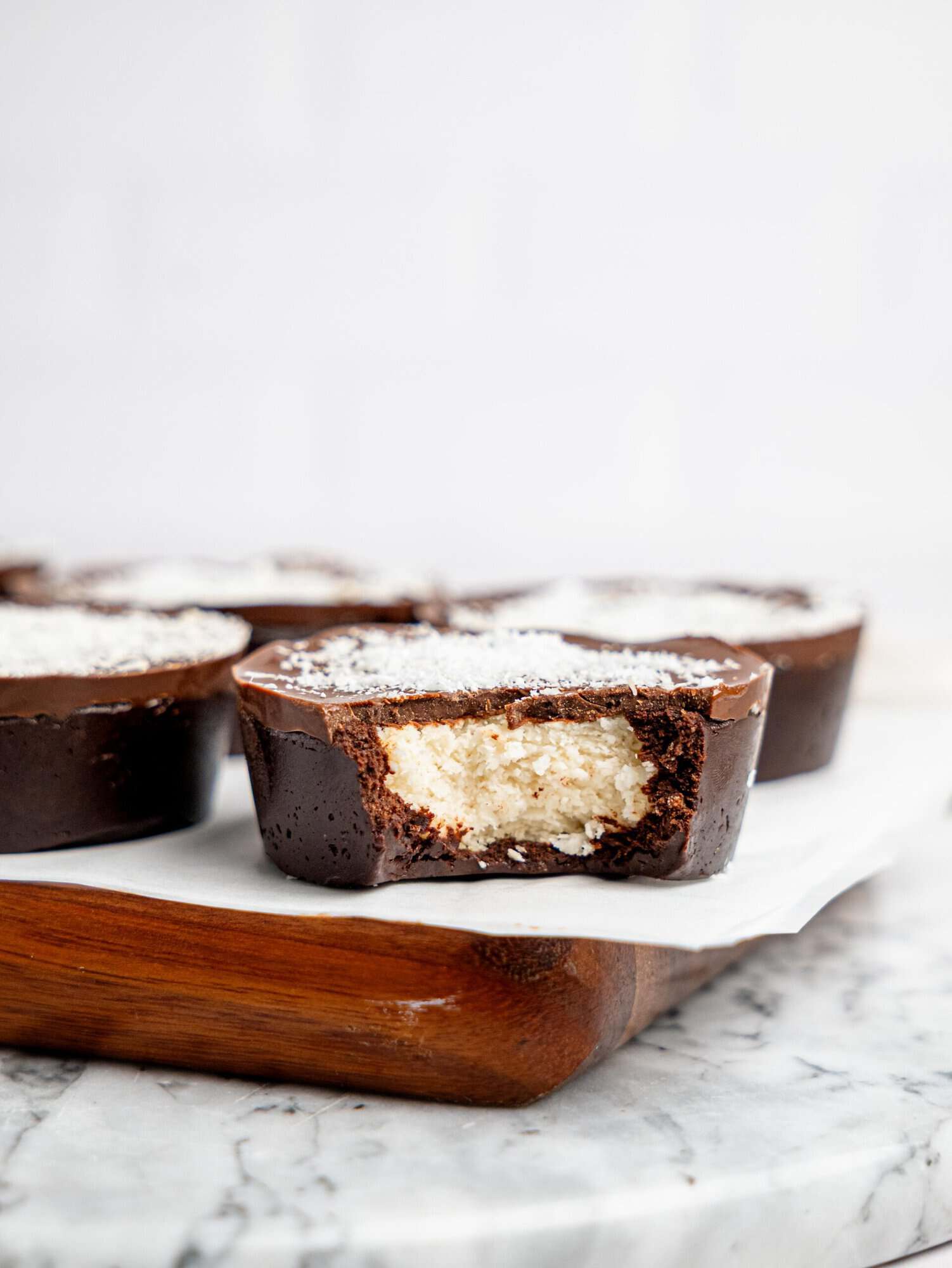 Chocolate brownie cup with a creamy coconut filling and dark chocolate topping, cut open to show the soft centre, sprinkled with desiccated coconut.