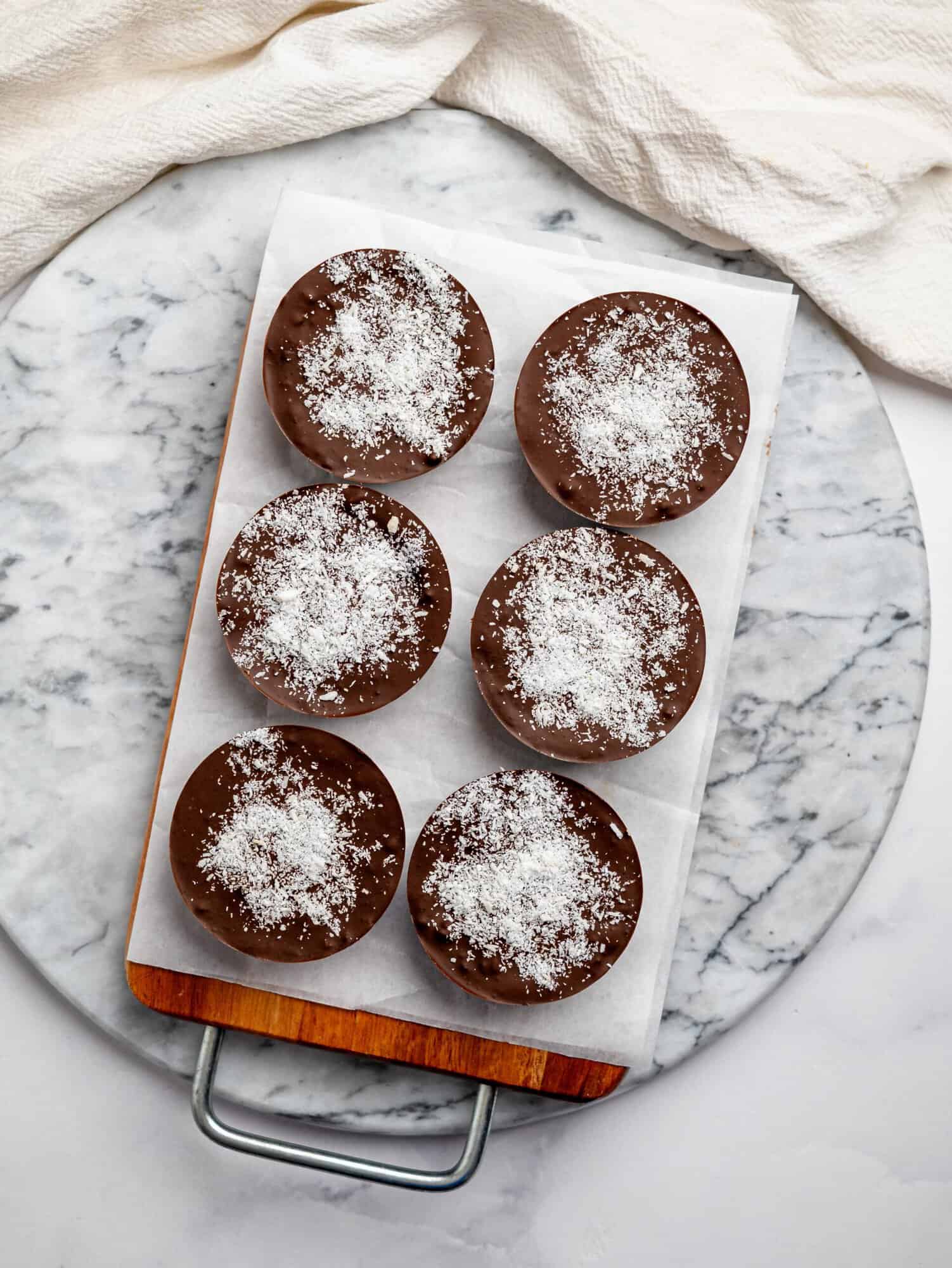 Chocolate brownie cups with a creamy coconut filling, topped with dark chocolate and a sprinkle of desiccated coconut, set on a wooden board.