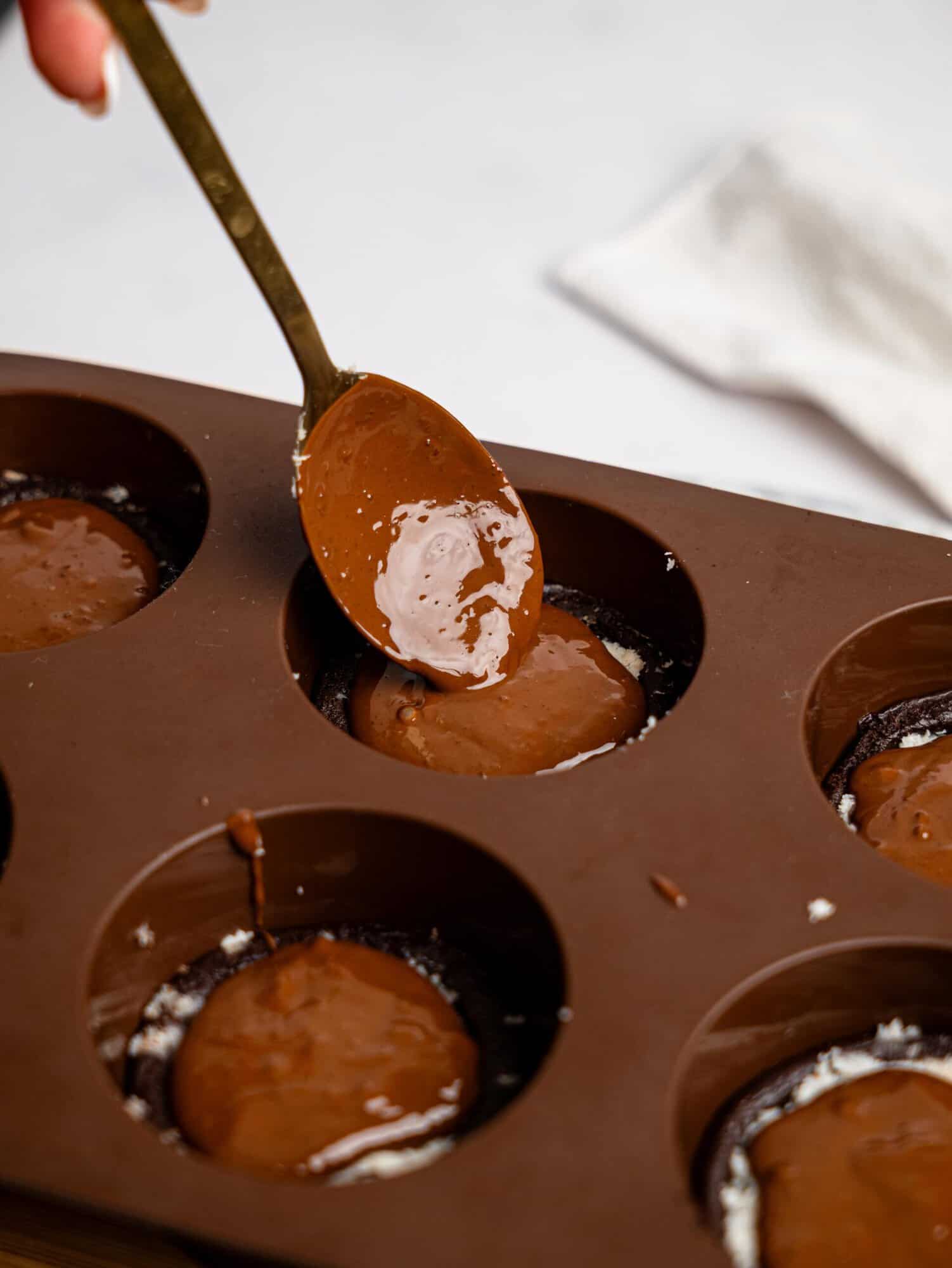 Adding melted dark chocolate onto a bounty brownie cup.