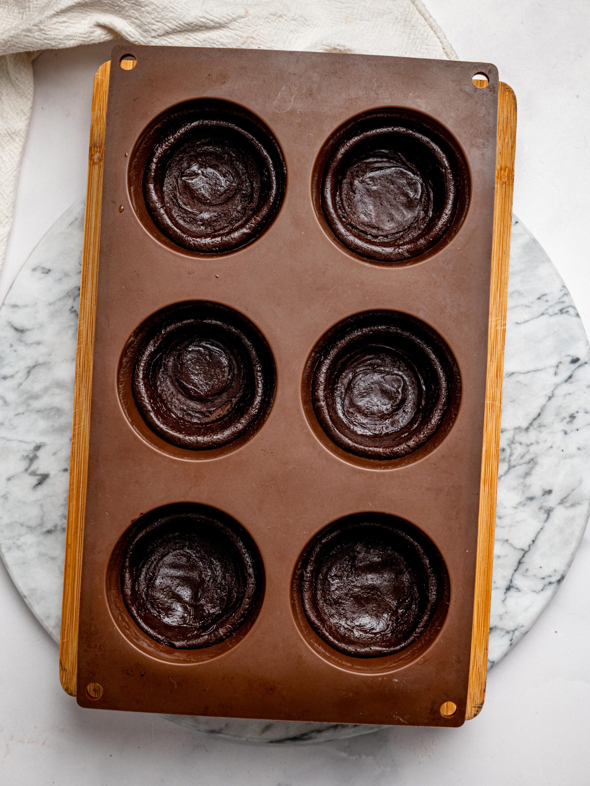 No bake chocolate brownie batter pressed into a brown silicone muffin tray to create "cups".