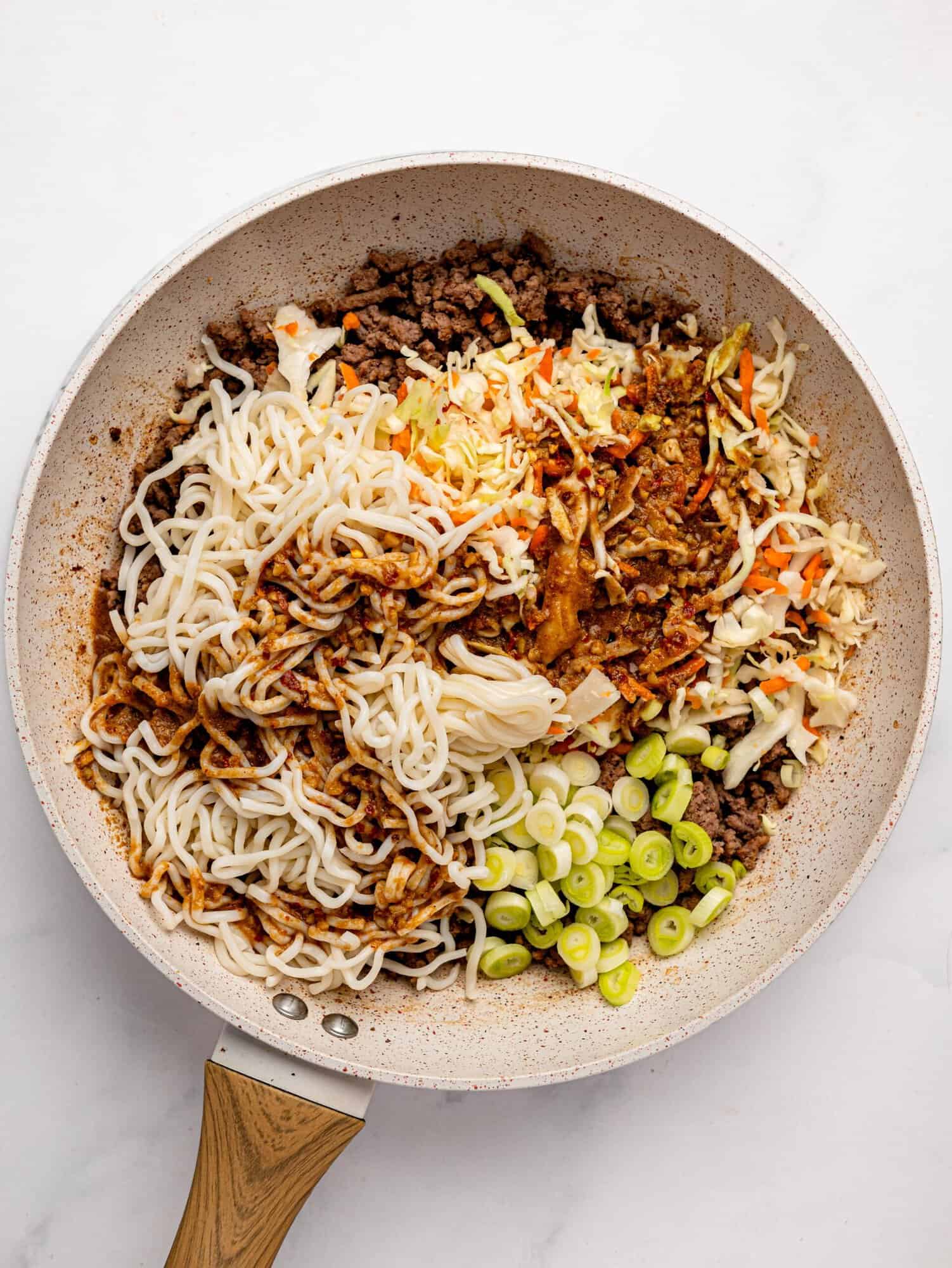 Spicy peanut butter noodles with ground beef ingredients in a frying pan.