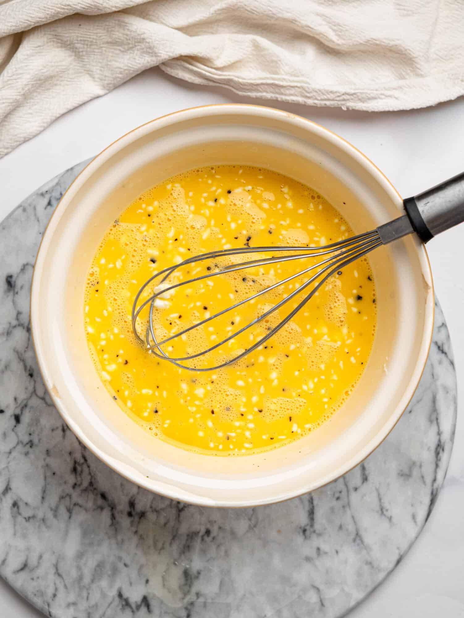 Bowl of whisked eggs with seasoning and cheese, ready to be combined with the spinach mixture.