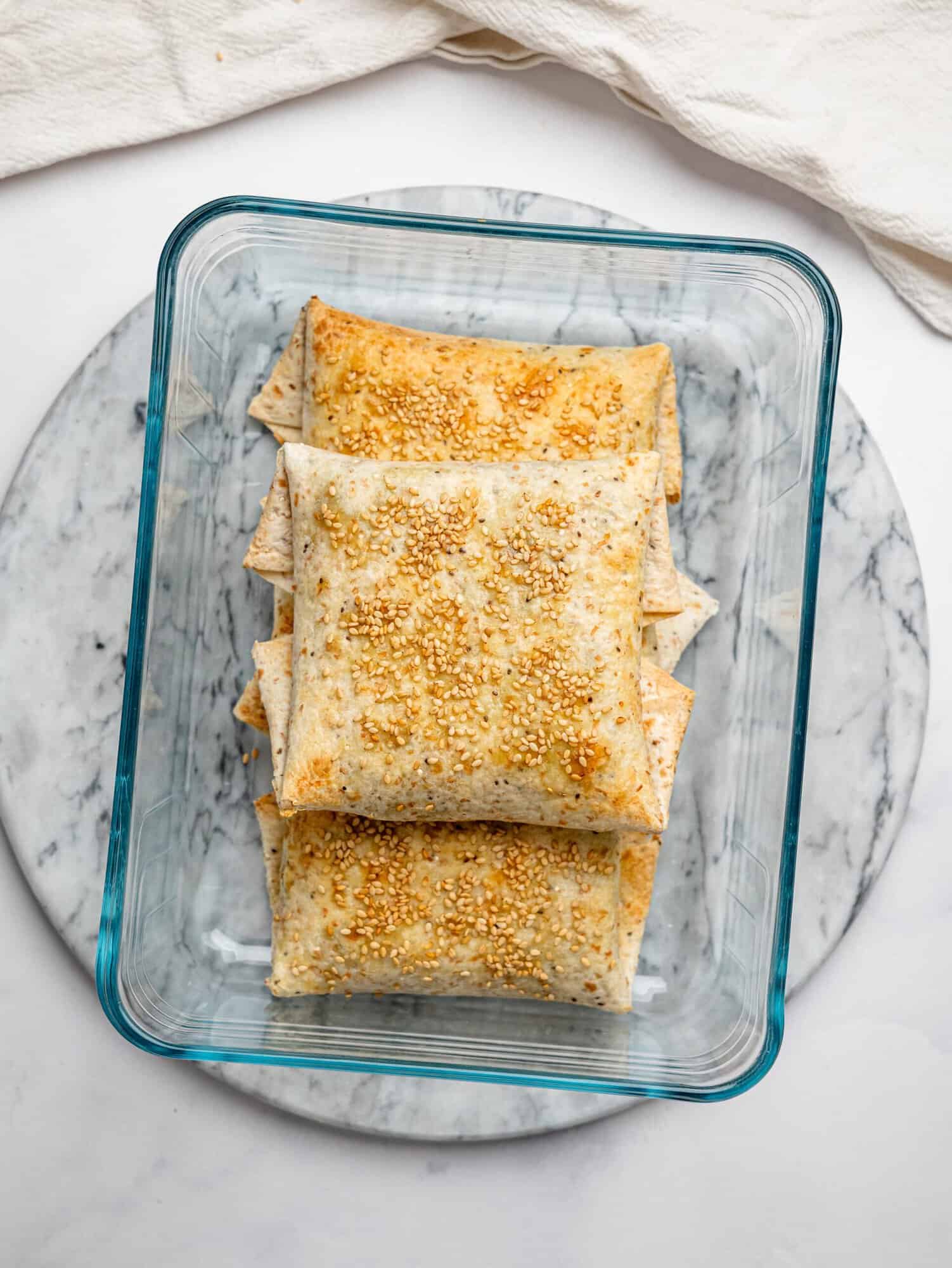 Meal prep container filled with multiple spanakopita egg wraps, stacked and ready for storage or grab-and-go meals.