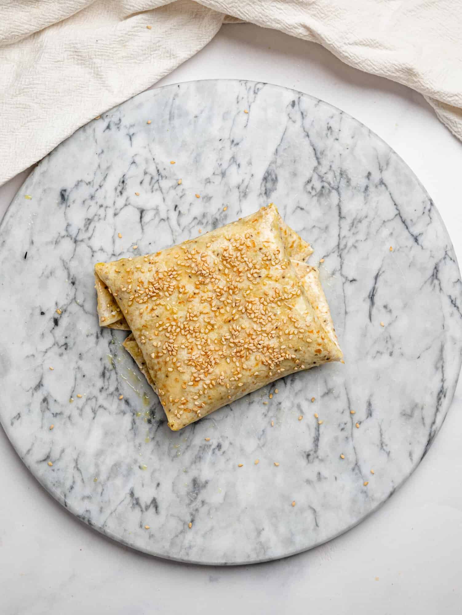 A tortilla folded over into a sealed wrap shape, brushed with olive oil and sprinkled with sesame seeds - ready to be air-fried.