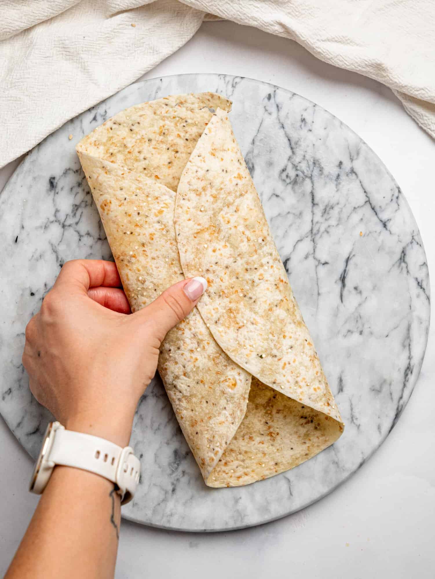 A tortilla folded over into a sealed wrap shape, held by hand, showing how the egg wrap is formed.