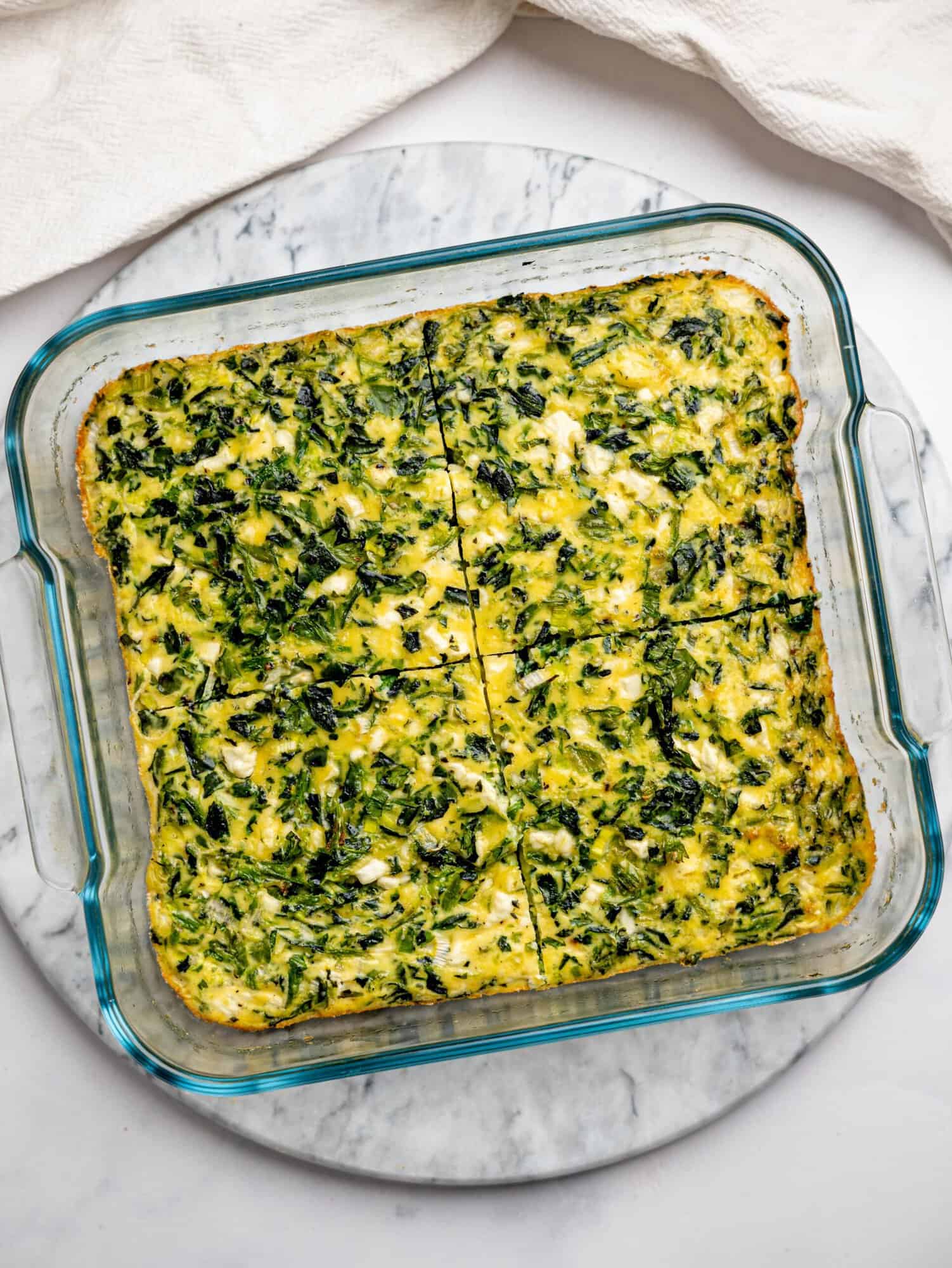 Baked spinach, feta, and egg mixture in a glass dish, sliced into even squares for assembling wraps.