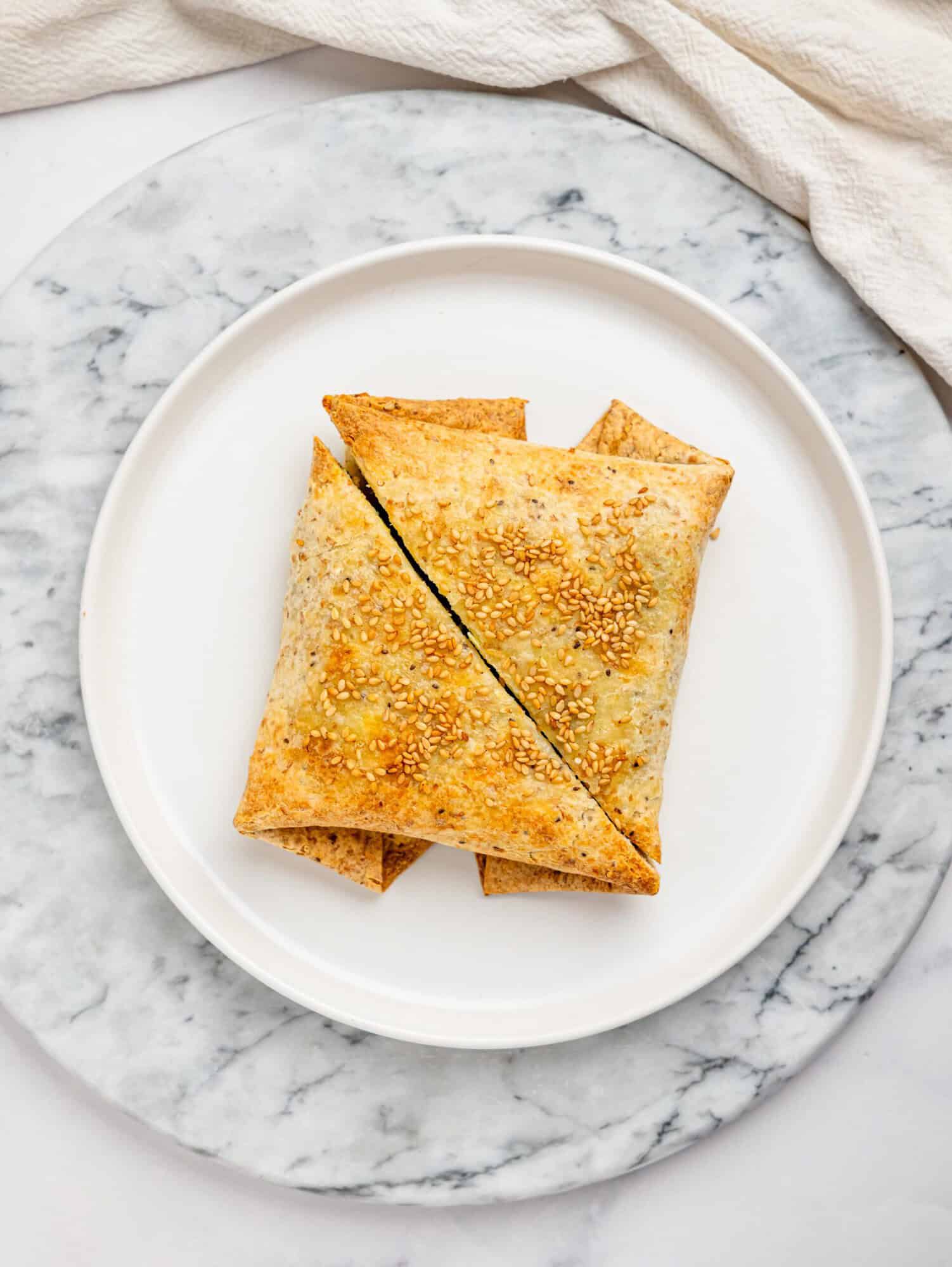 Close-up overhead of two sesame-topped spanakopita egg wraps cut into triangles, highlighting their crisp edges.