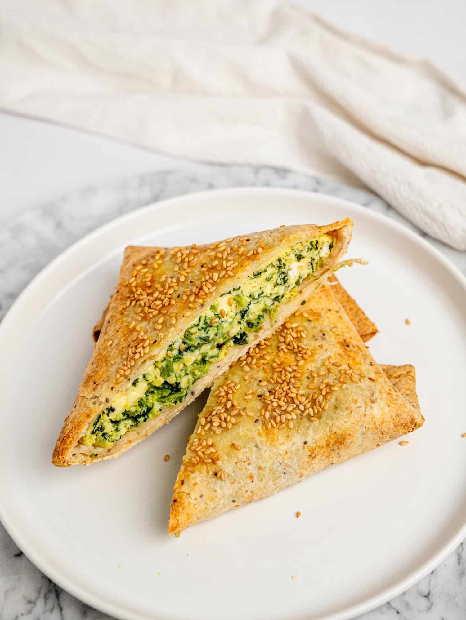Two toasted spanakopita egg wraps on a white plate, cut open to show the soft, herby spinach and feta egg filling inside the crispy tortilla.