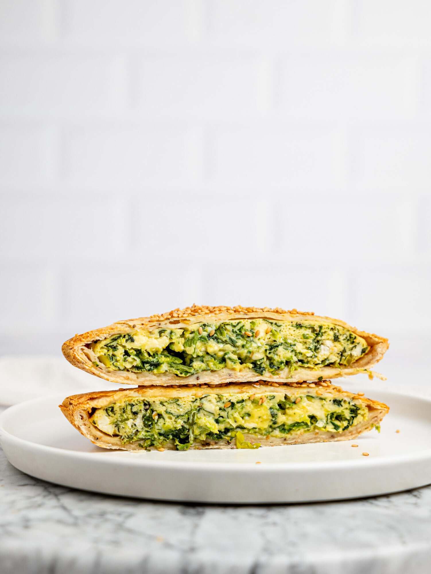 Side view of a sliced spanakopita egg wrap stacked on a plate, showing the thick, fluffy egg filling packed with spinach and feta.