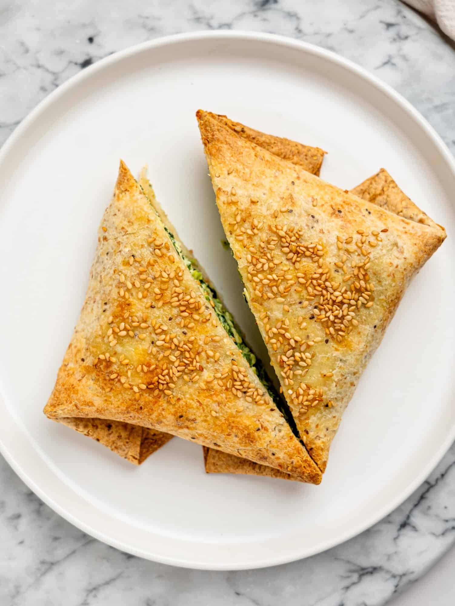 Overhead shot of stacked spanakopita egg wraps on a plate, showing their evenly toasted, golden tortilla exterior.