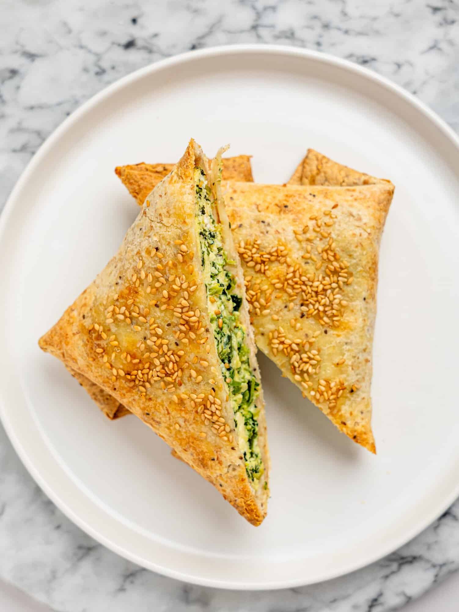 Close-up overhead of two sesame-topped spanakopita egg wraps cut into triangles, highlighting their crisp edges.