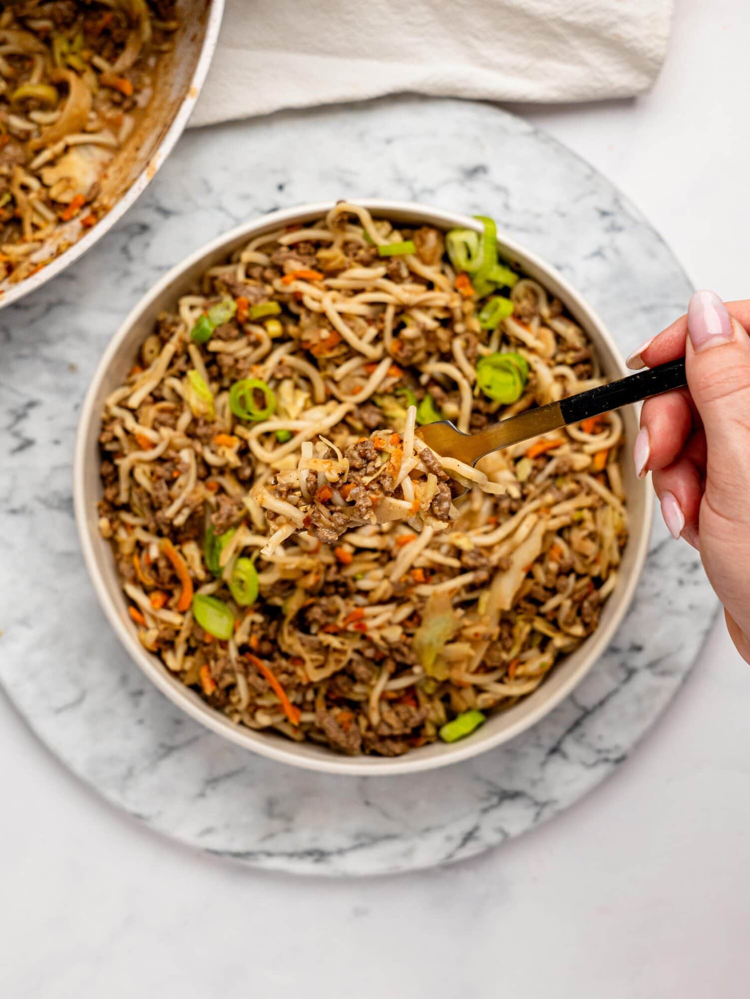 Spicy peanut butter noodles, ground beef, and vegetables in a white bowl.