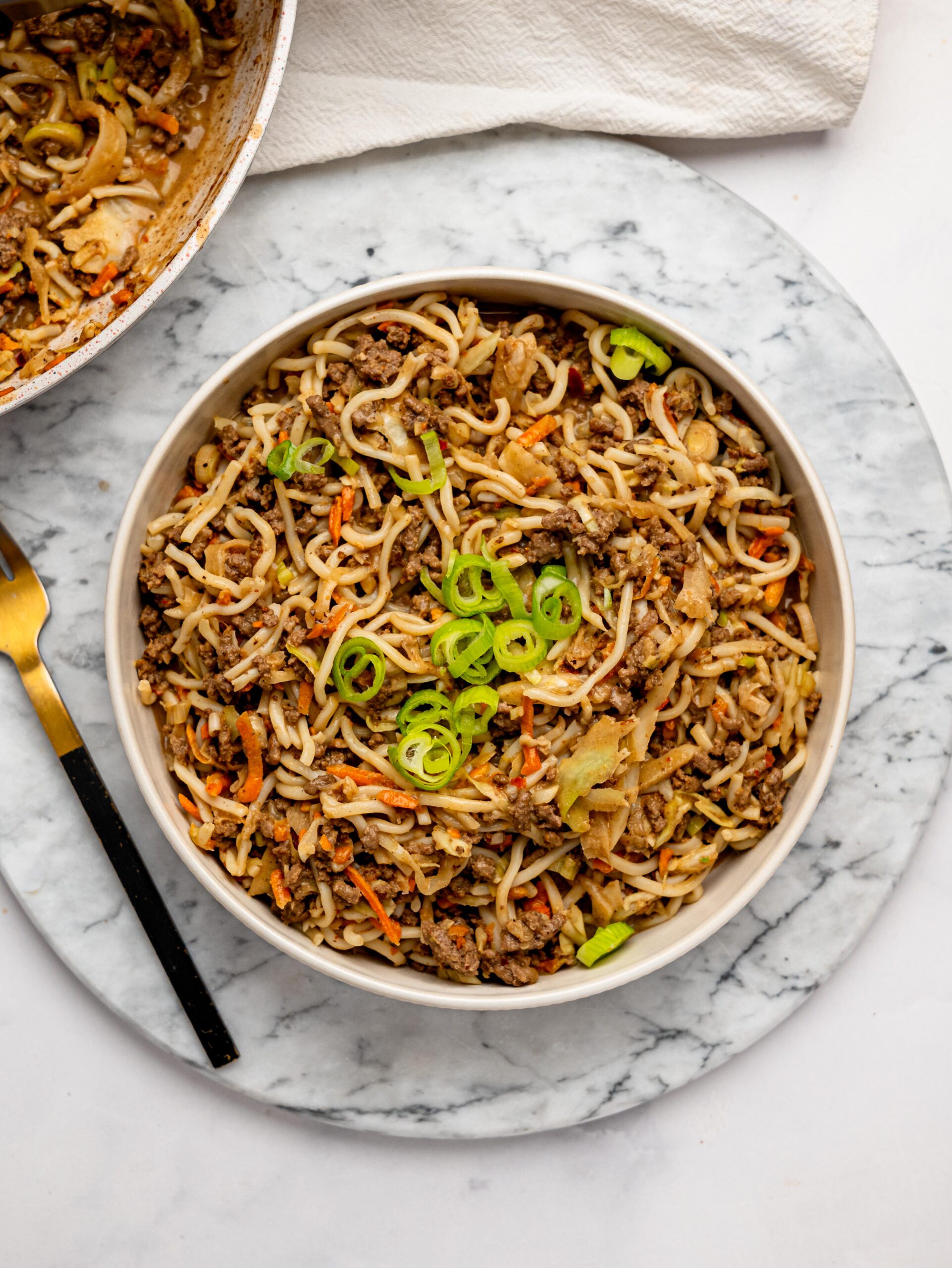 Spicy peanut butter noodles, ground beef, and vegetables in a white bowl.