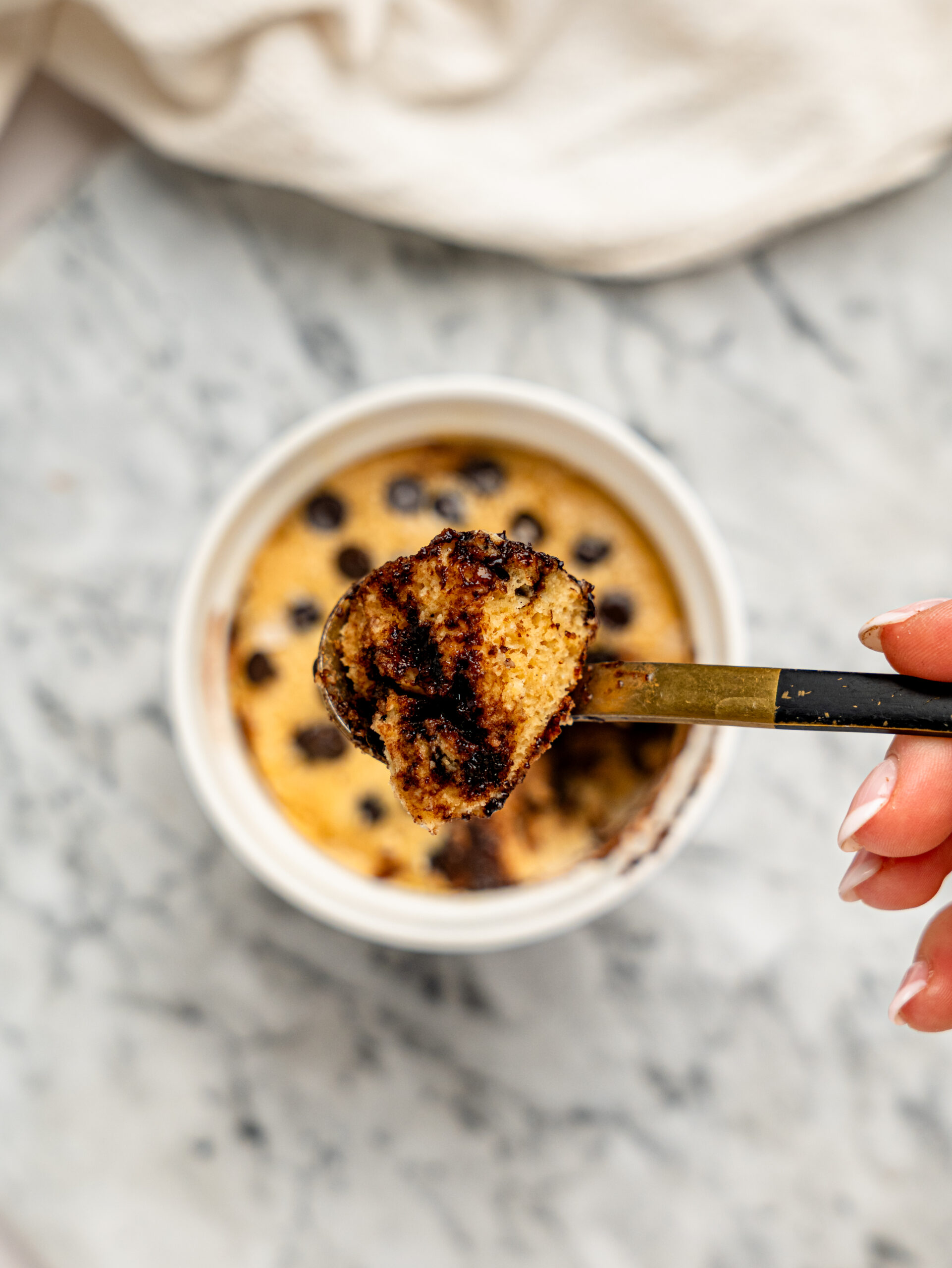 Spoonful of fluffy protein mug cake with melted chocolate chips held above the ramekin.