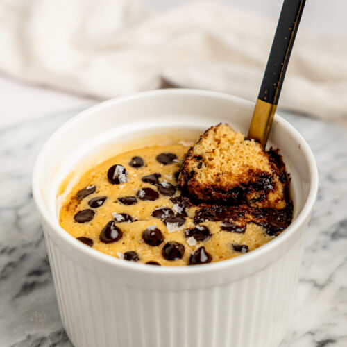 Close-up of a healthy chocolate chip protein mug cake with a spoon scooping out a warm bite of cake and melted chocolate.