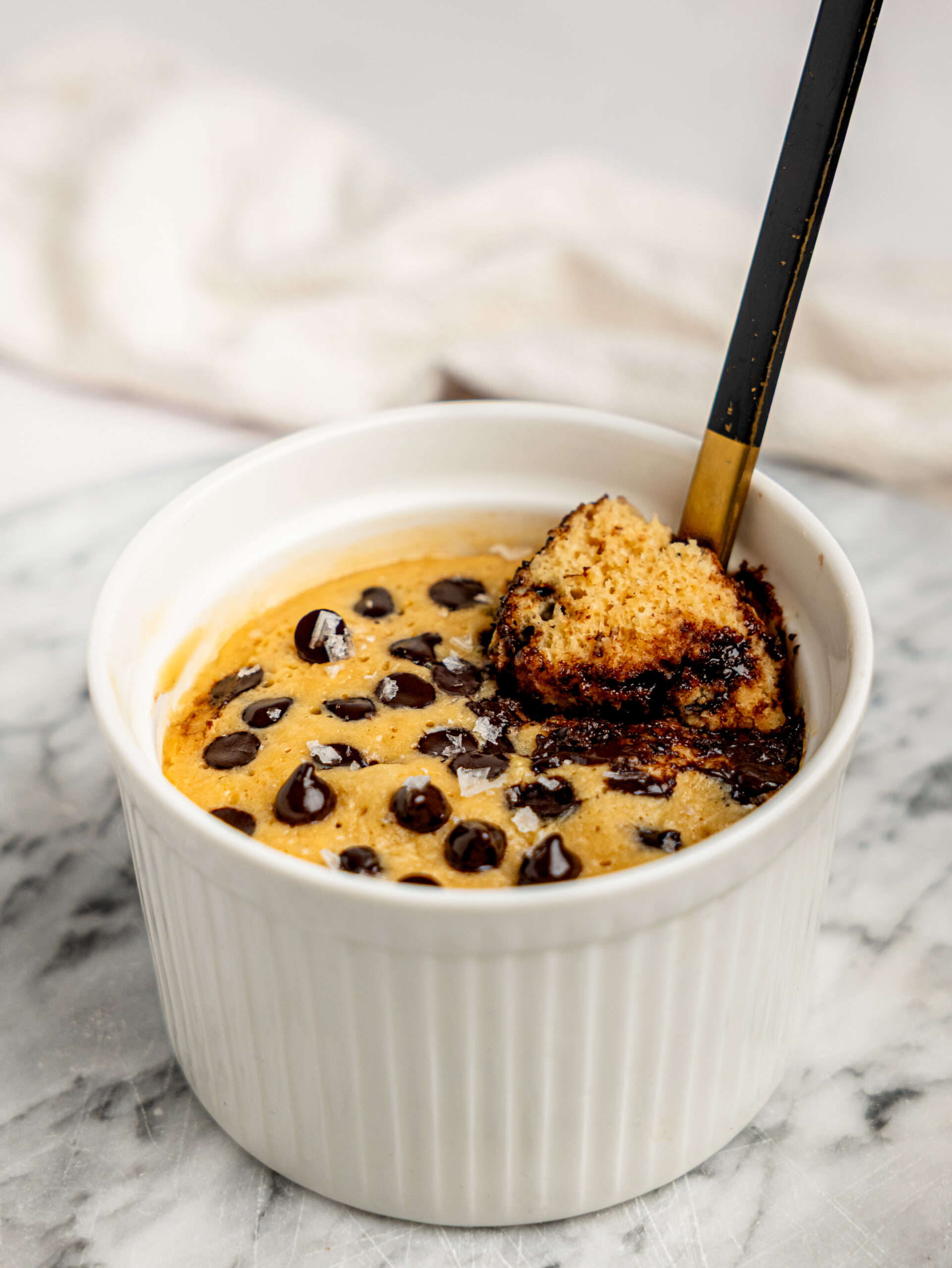 Close-up of a healthy chocolate chip protein mug cake with a spoon scooping out a warm bite of cake and melted chocolate.