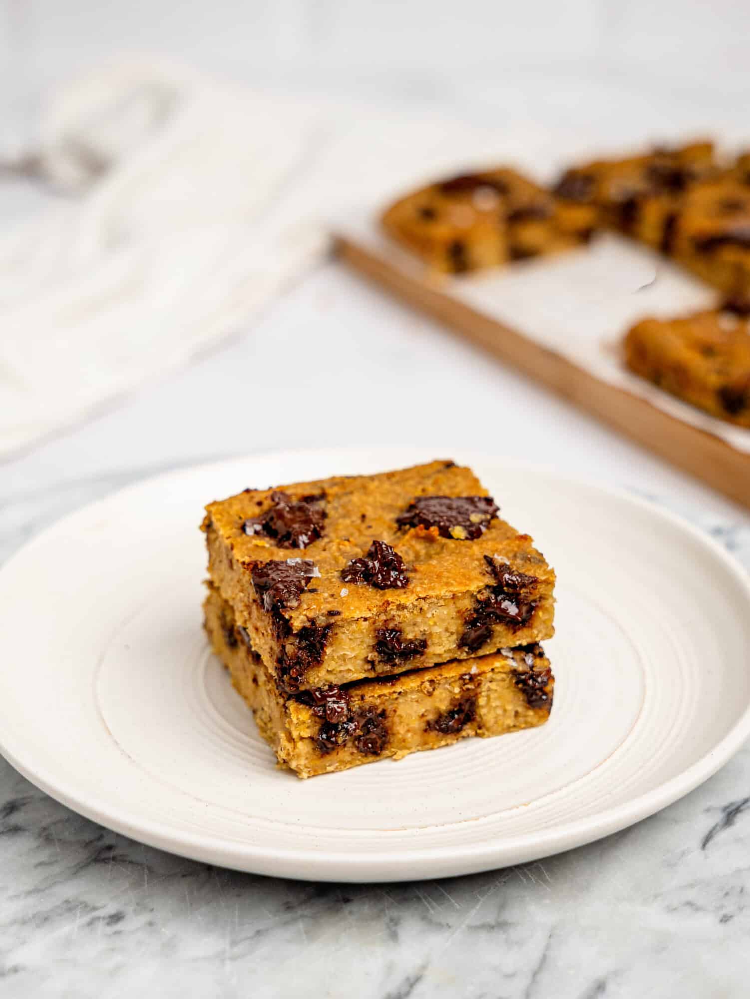 Two chickpea cookie bars stacked on top of each other on a white plate.