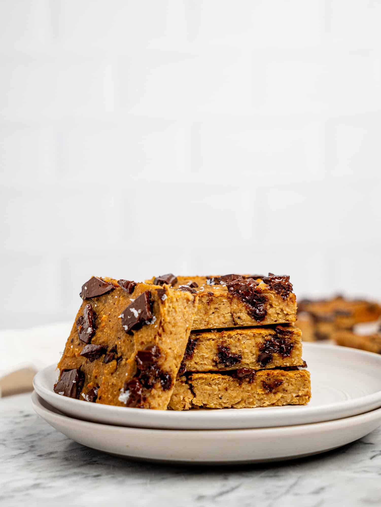 Healthy cookie bars with dark chocolate stacked on a white plate.