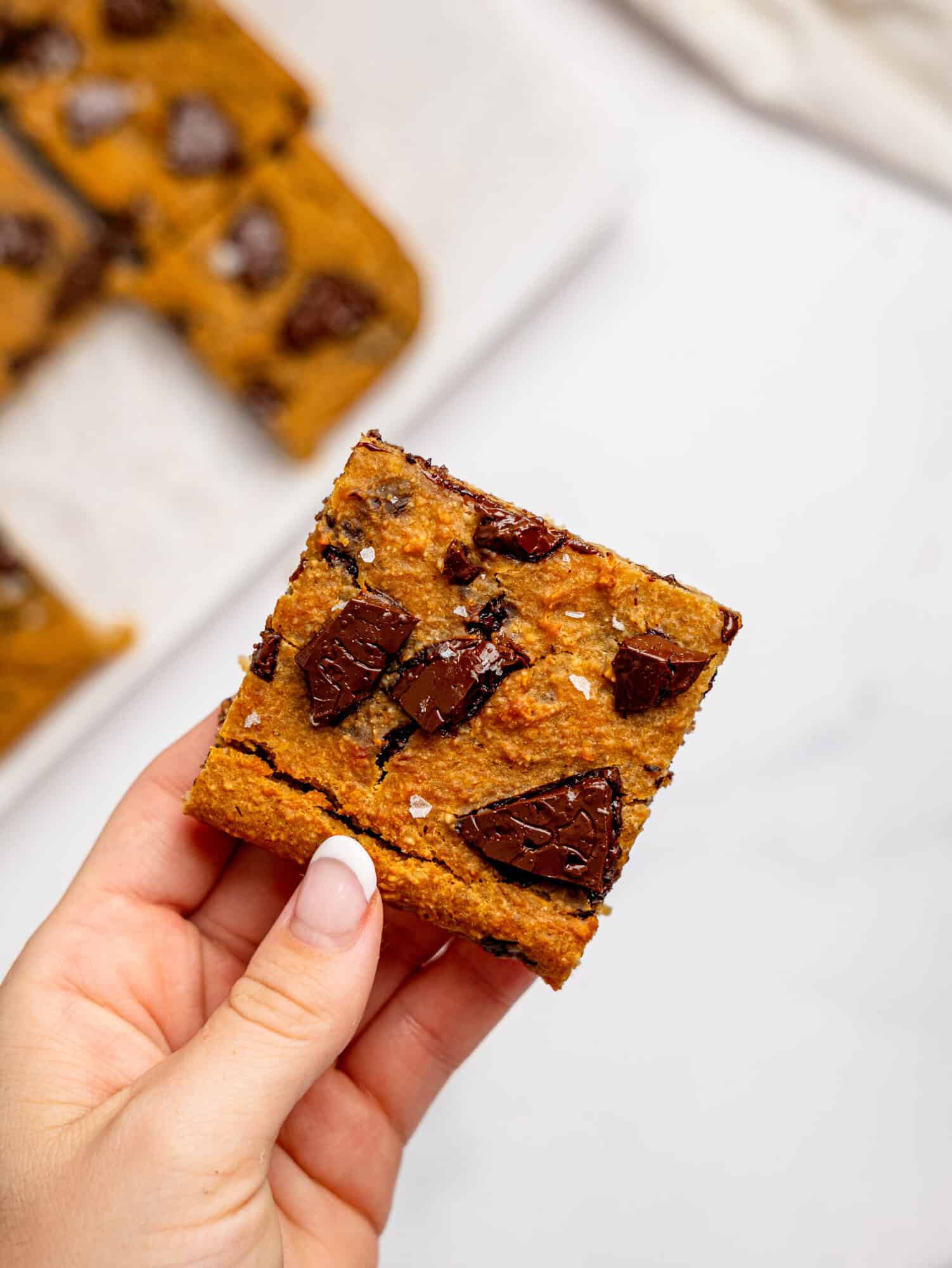 A hand holding a chickpea cookie bar with dark chocolate.