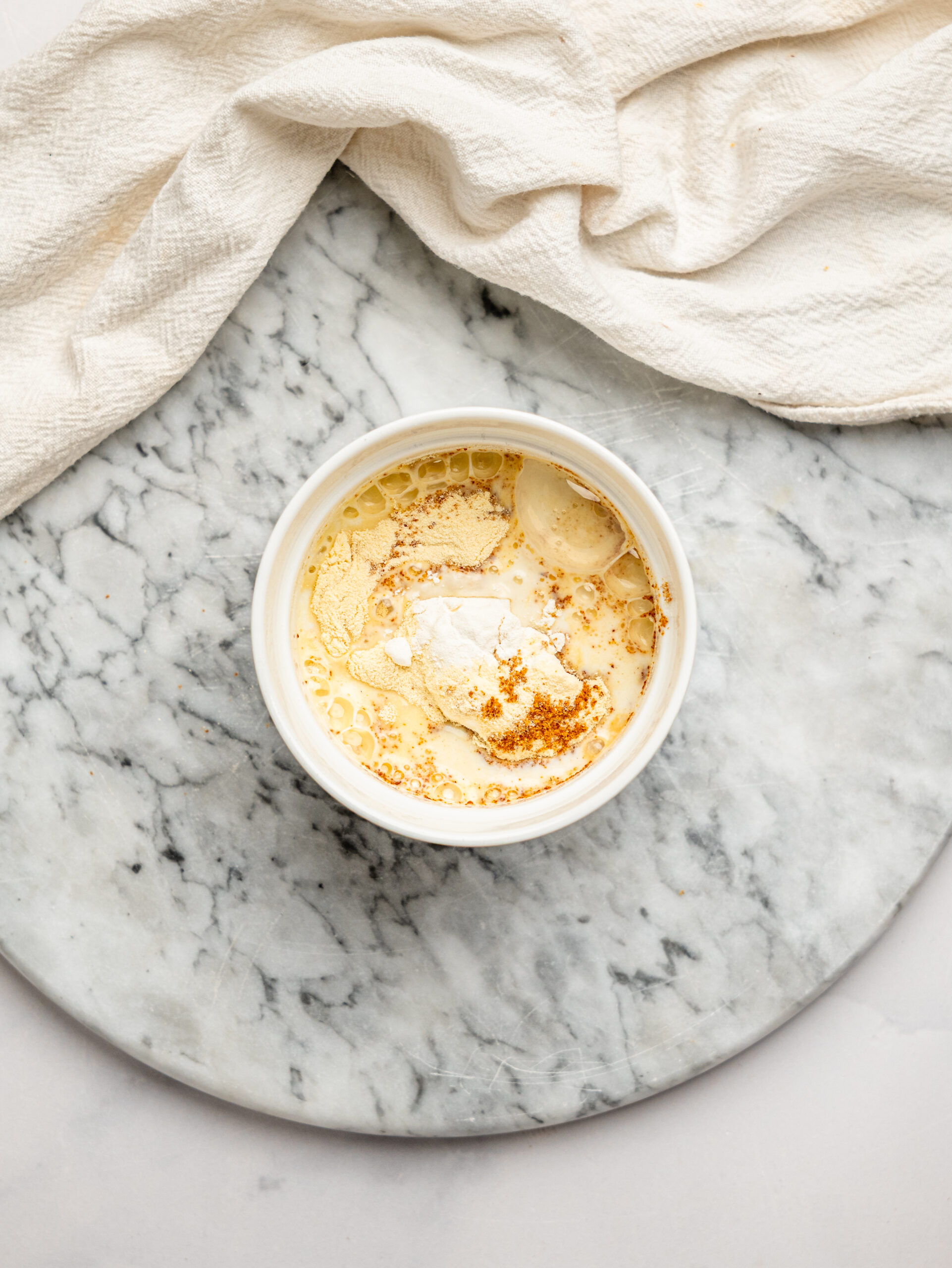 Ingredients for a healthy chocolate chip protein mug cake combined in a ramekin before mixing, including protein powder, flour, and milk.