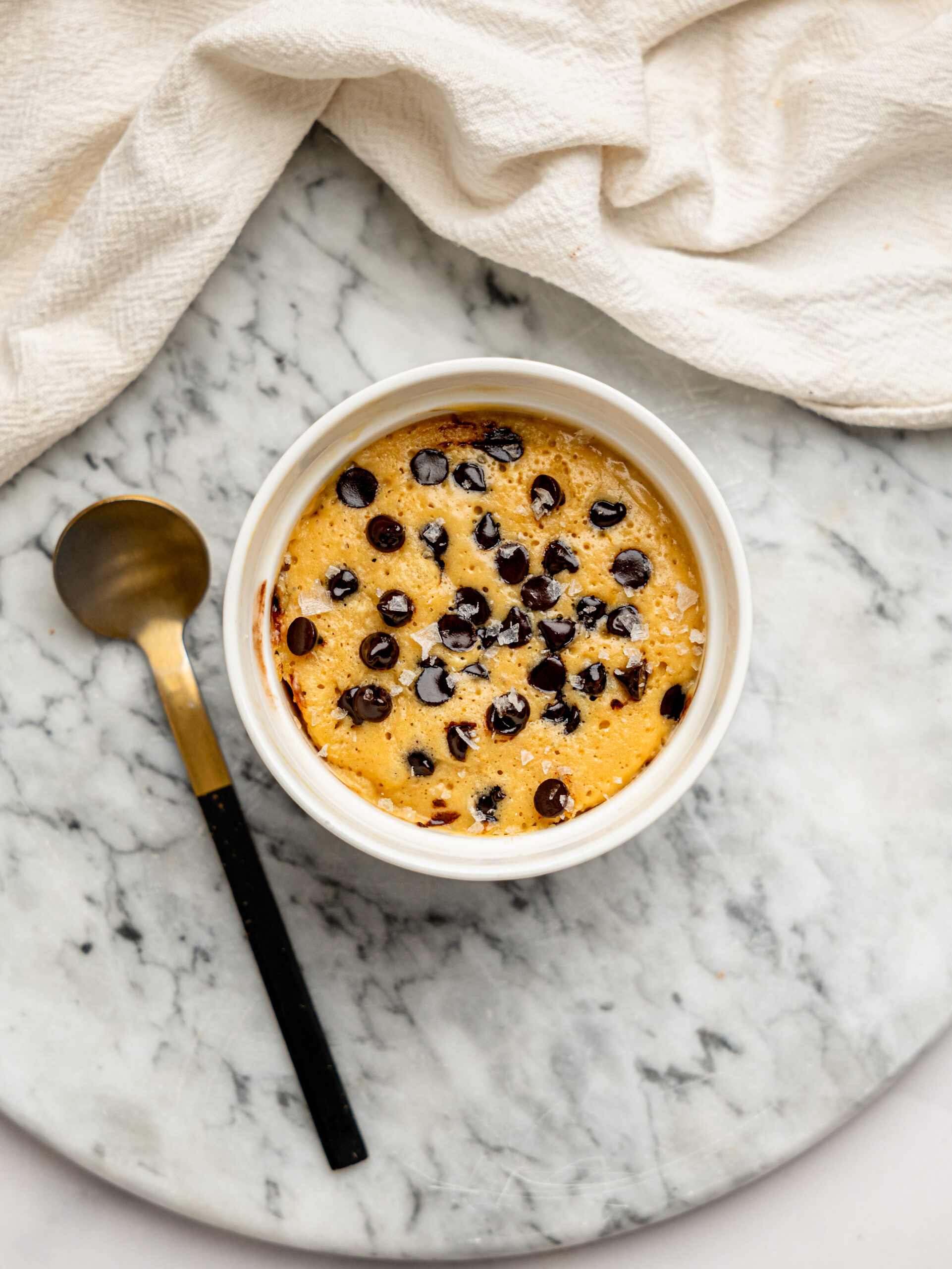 Overhead photo of a baked healthy chocolate chip mug cake topped with dark chocolate chips and flaky sea salt.