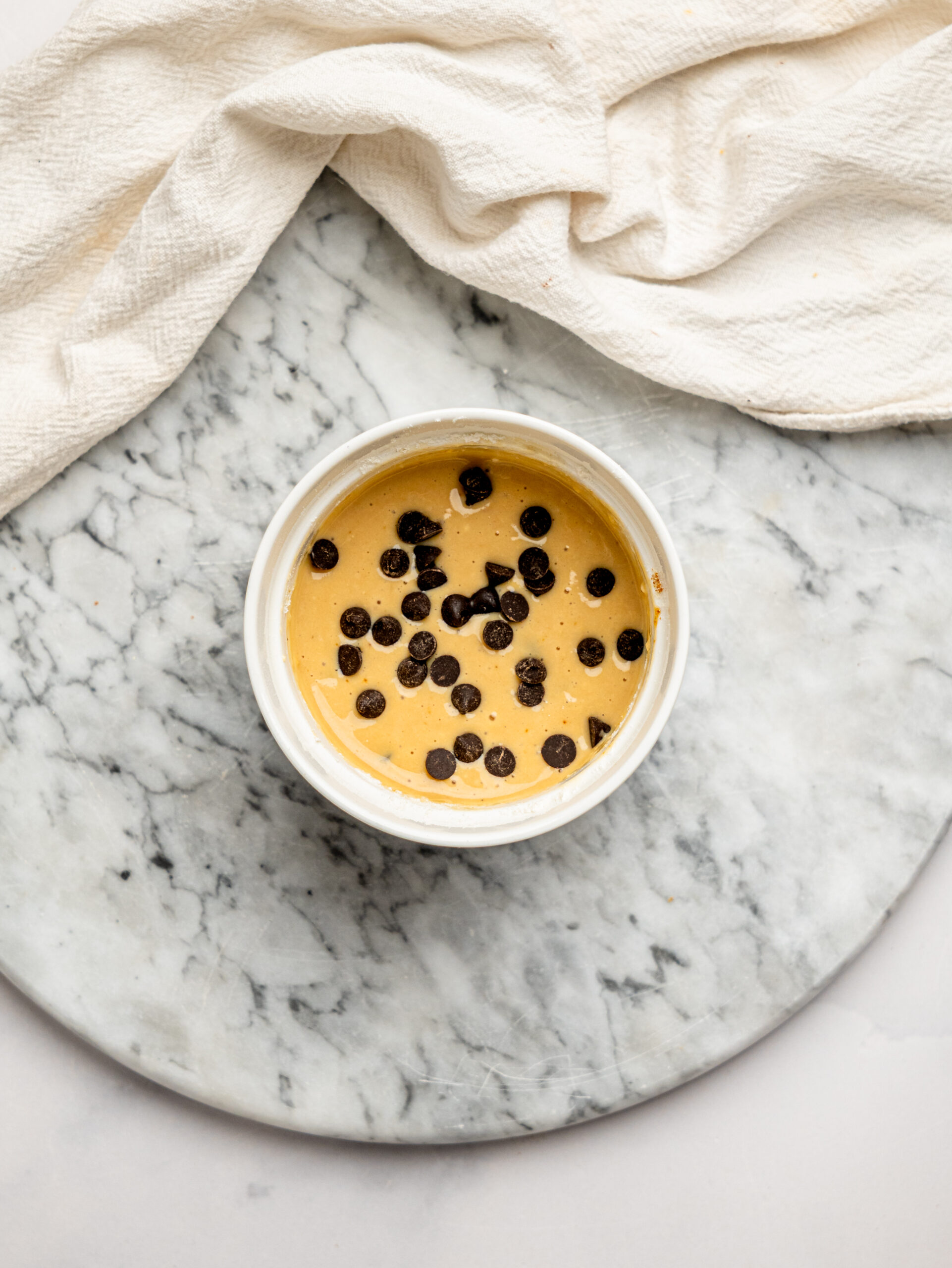 Unbaked chocolate chip protein mug cake batter in a ramekin topped with dark chocolate chips before cooking.