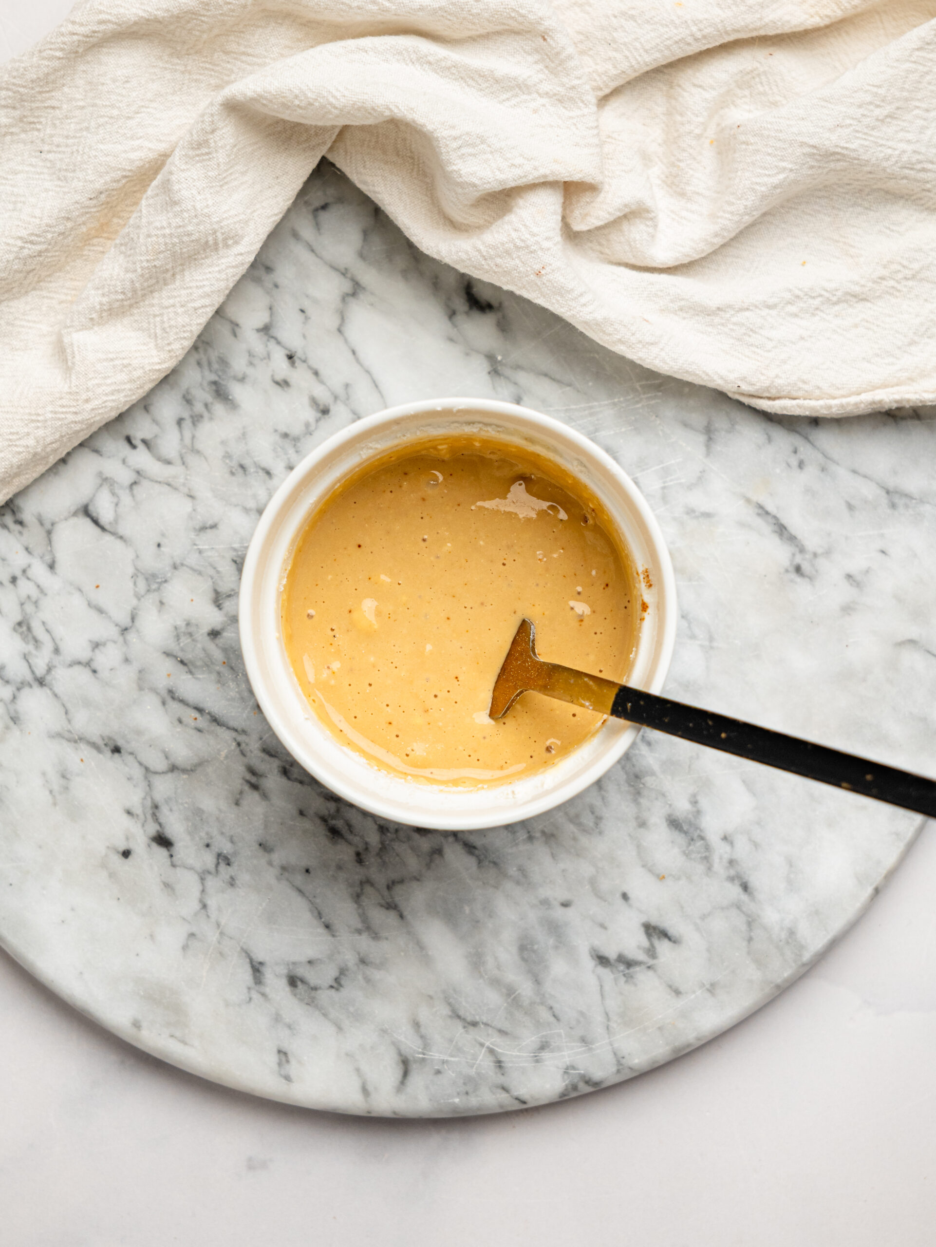 Smooth vanilla protein mug cake batter being stirred in a white ramekin with a spoon.
