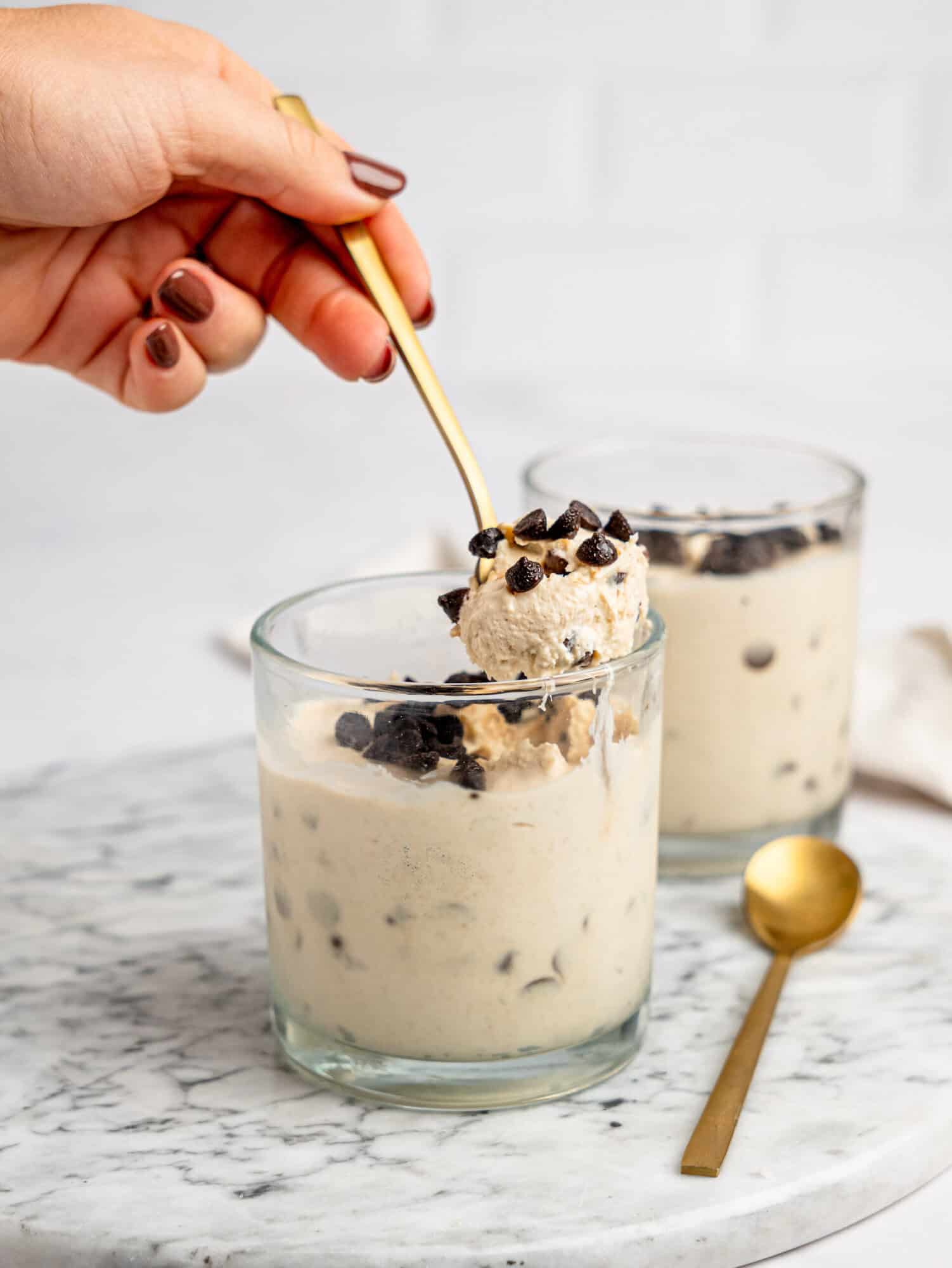 High-protein Cottage Cheese Cookie Dough Mousse in glass cups topped with chocolate chips and served on a marble board.