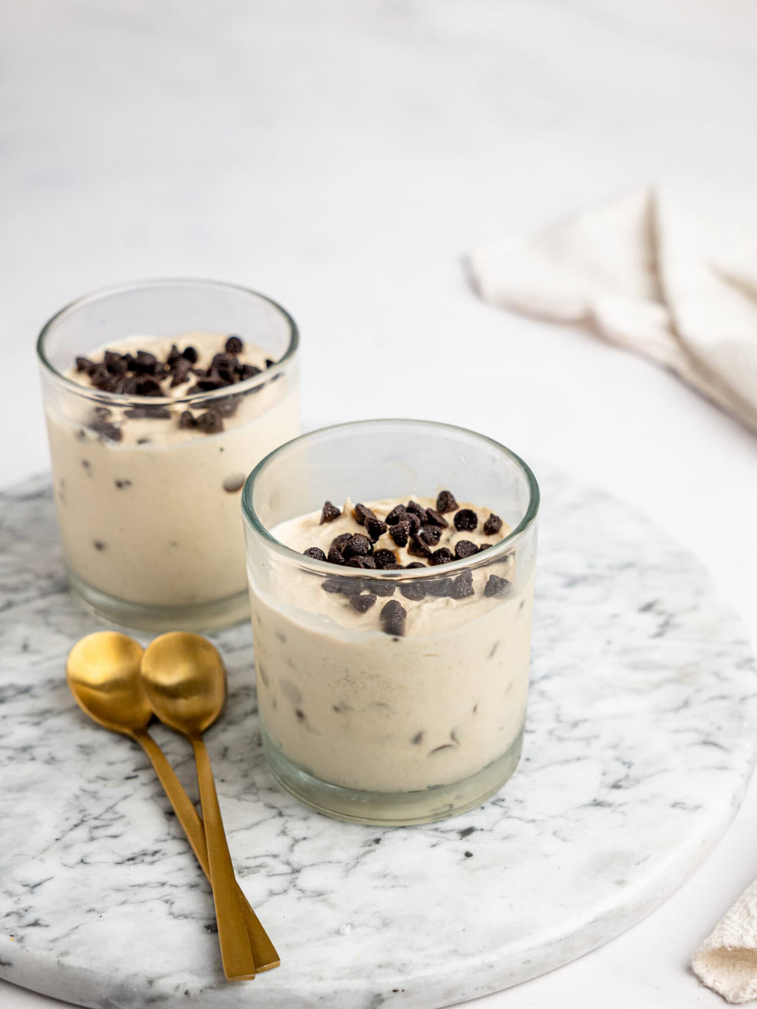 Two servings of Cottage Cheese Cookie Dough Mousse topped with dark chocolate chips and served with gold dessert spoons.