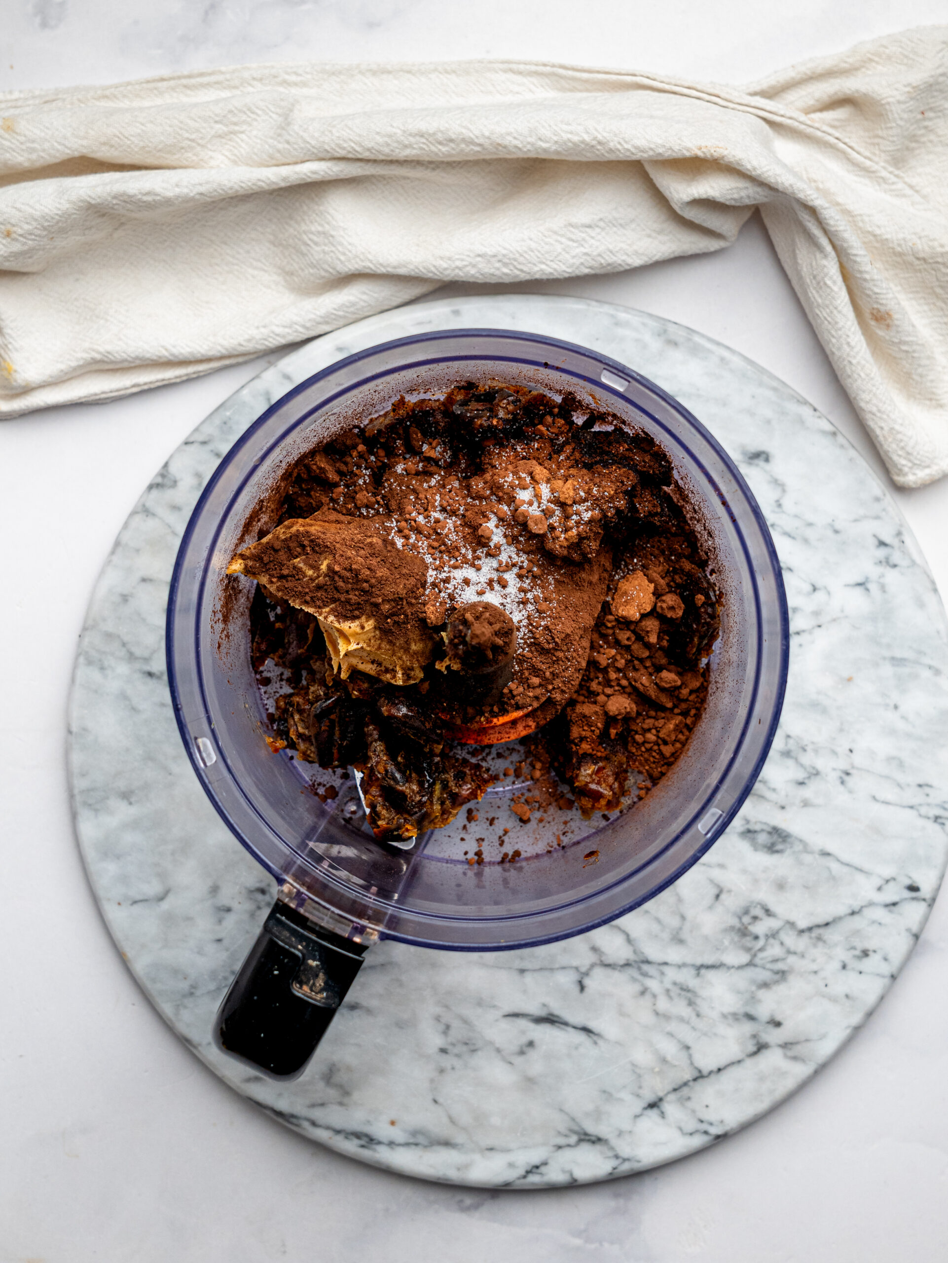 Dates, cocoa powder, nut butter, vanilla, and salt added to a food processor to make no-bake brownie bites.