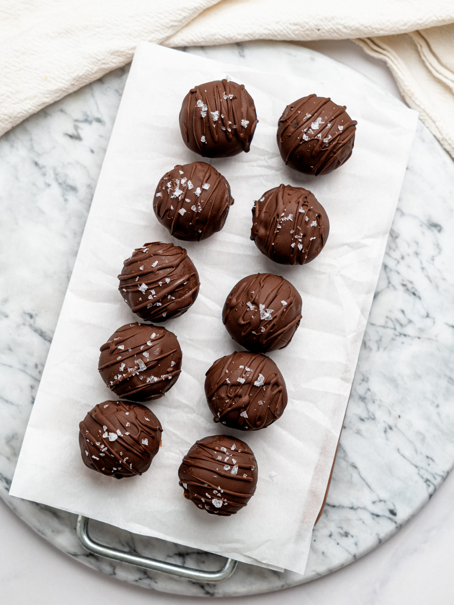 Overhead view of chocolate-covered no-bake brownie bites arranged on parchment paper and sprinkled with flaky sea salt.
