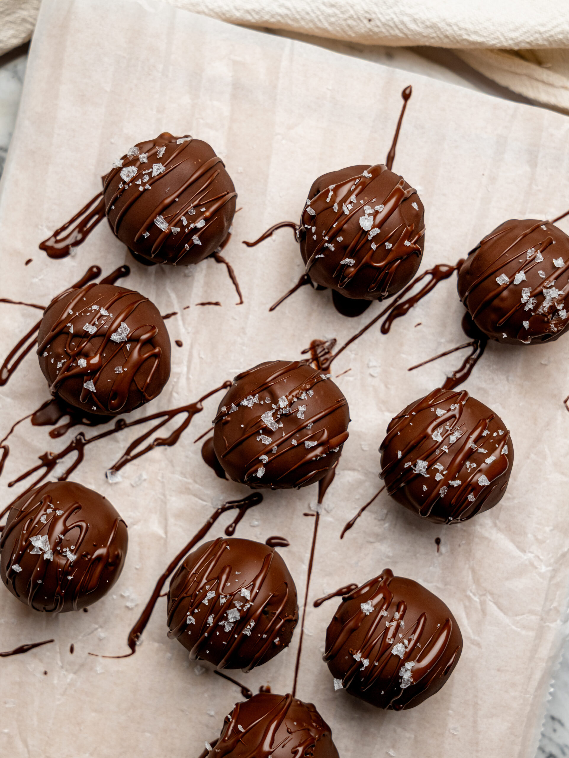 Close-up of chocolate brownie bites on parchment paper with dark chocolate drizzle and flaky sea salt.