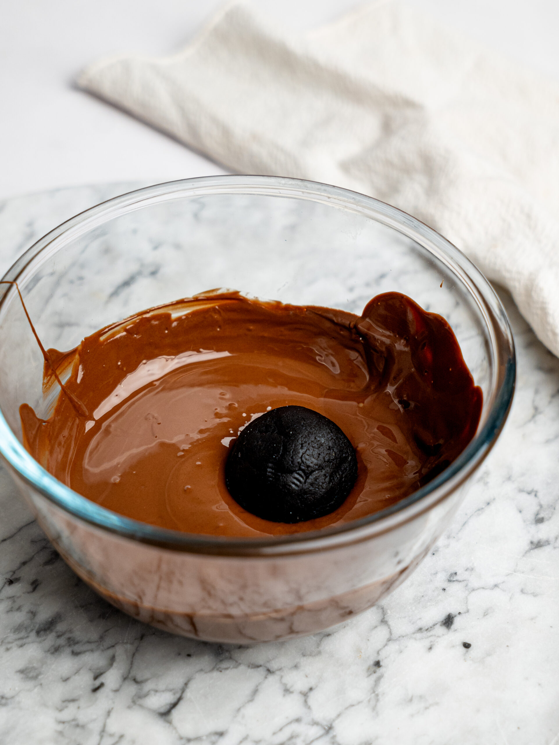 Brownie bite being dipped into melted dark chocolate in a glass bowl.