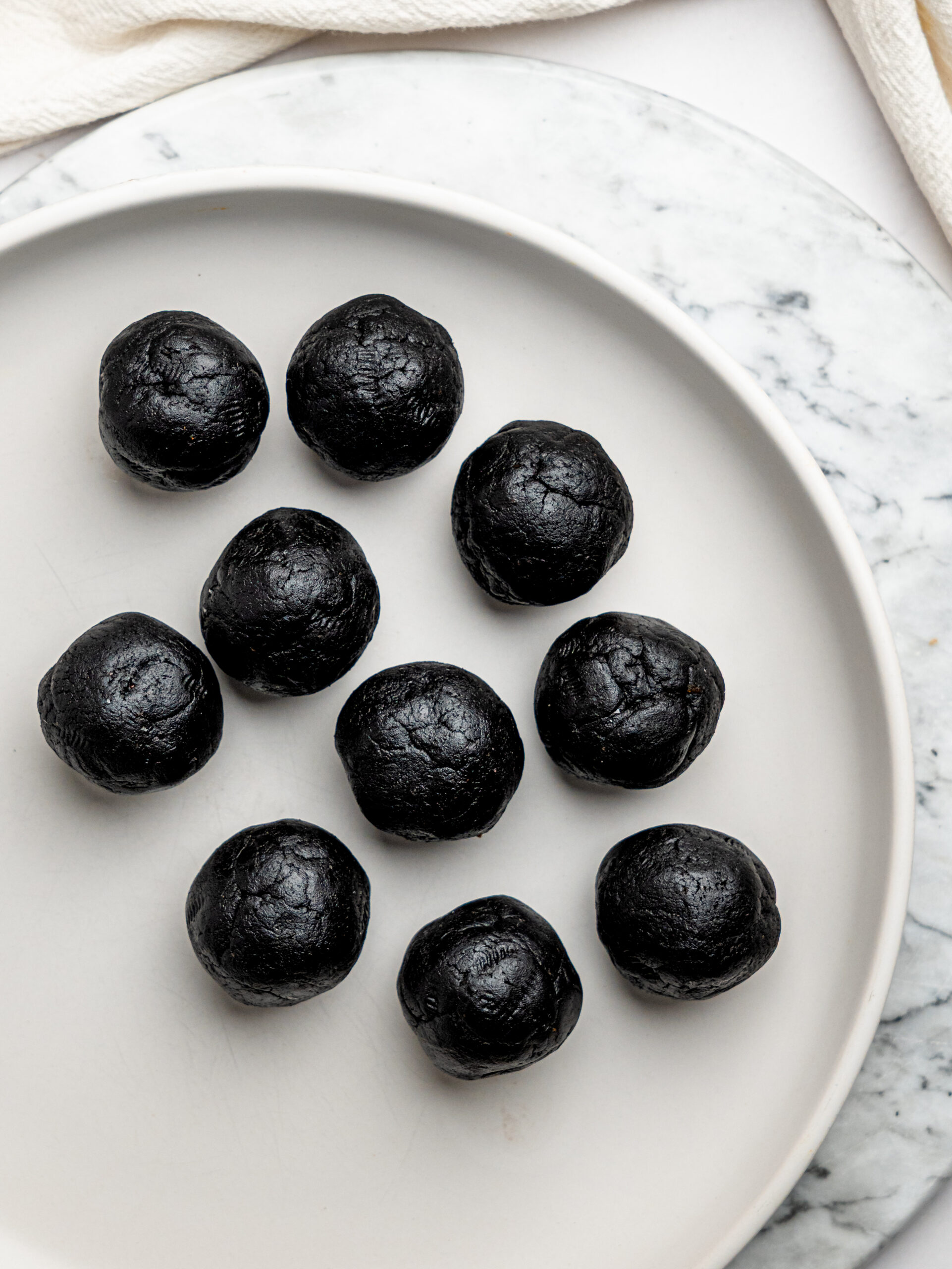 Chocolate brownie bite mixture rolled into smooth balls and arranged on a white plate before coating.