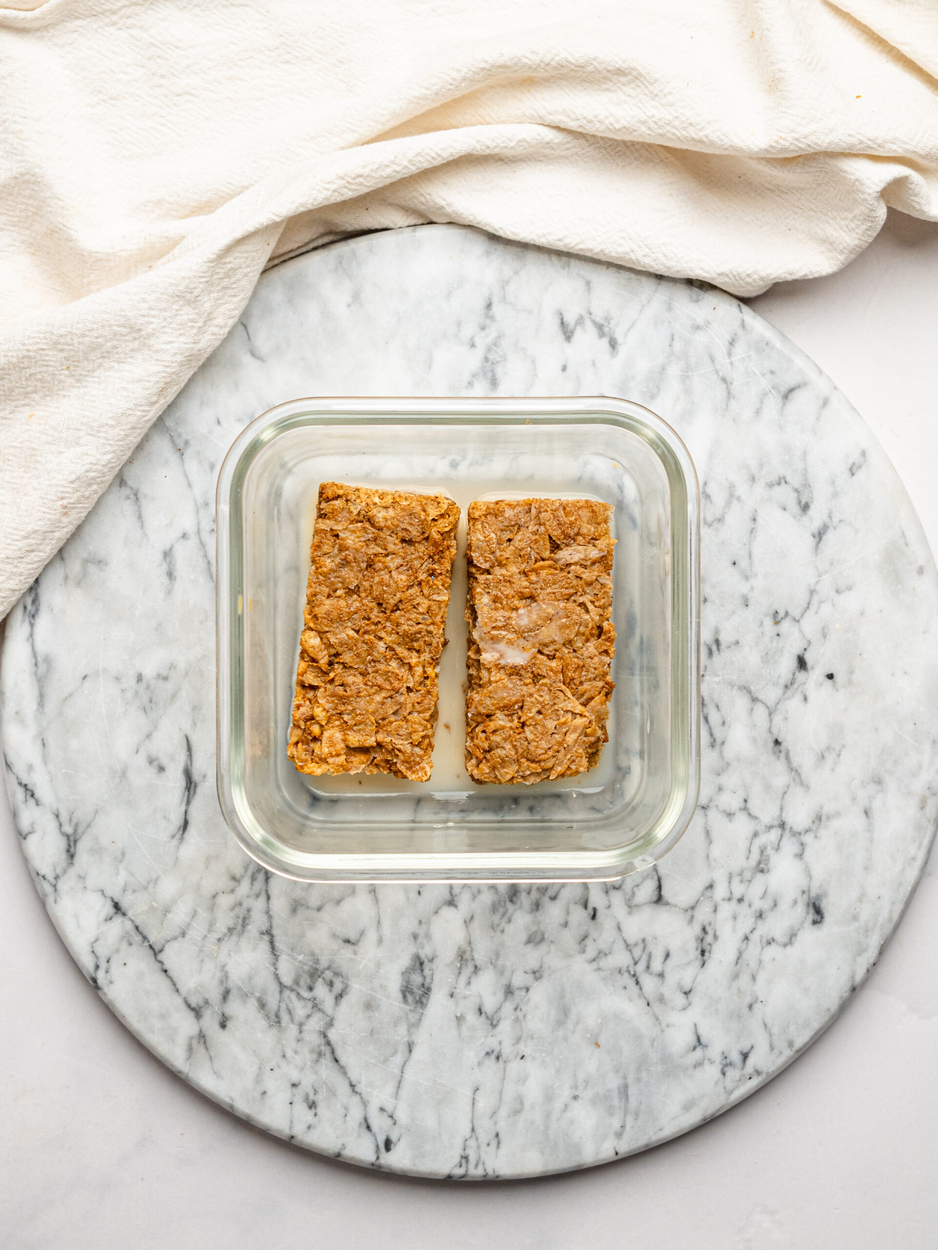 Weet-Bix biscuits and milk in a glass meal-prep container, ready to form the base of this Lemon Cheesecake Ovenight Weet-Bix.