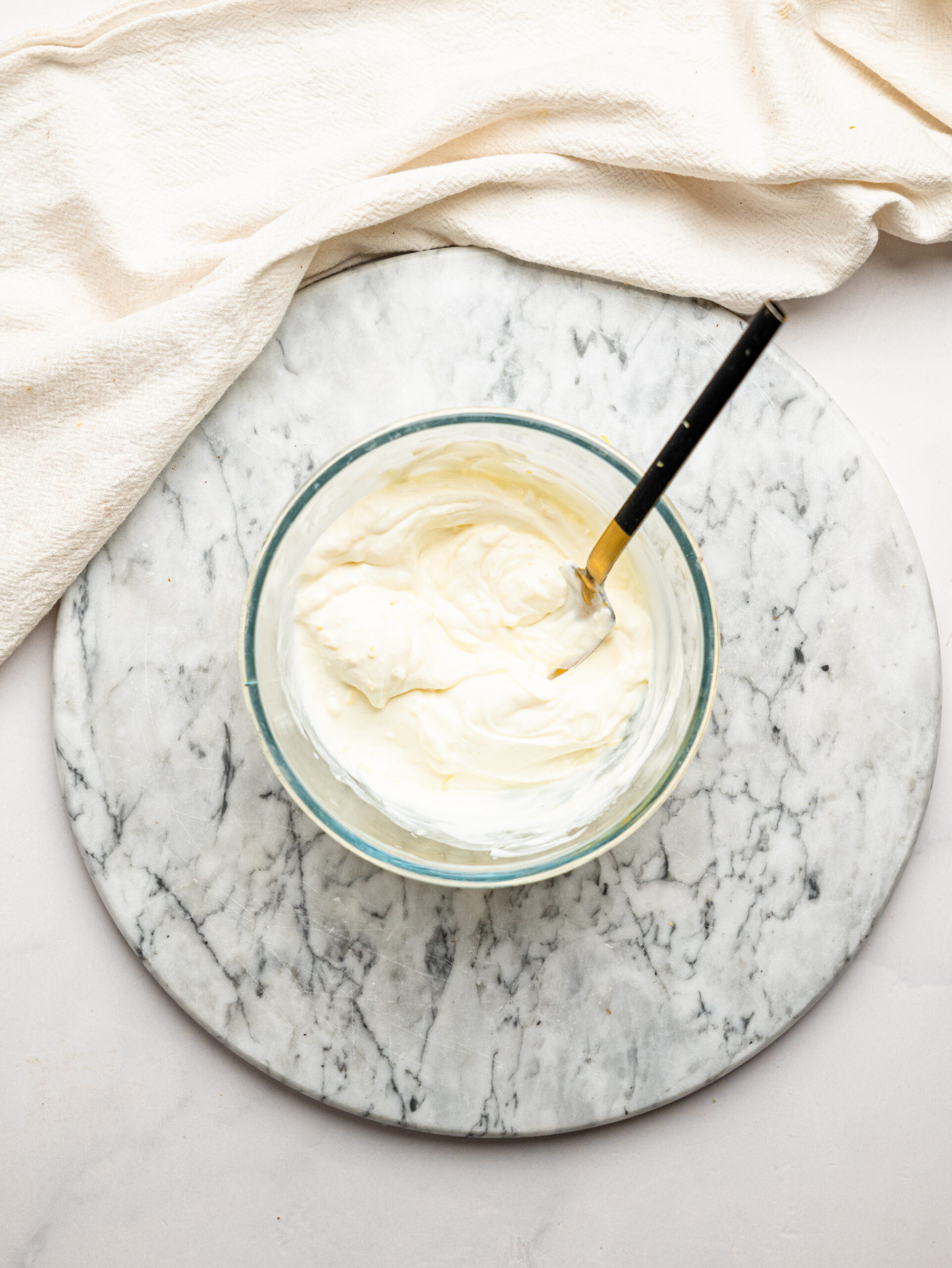 Smooth and creamy lemon cheesecake filling mixed in a glass bowl with a spoon.