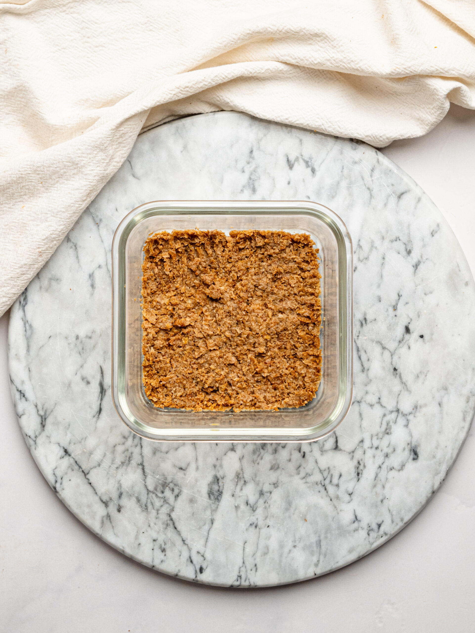 Crushed Weet-Bix mixed with milk and pressed into a glass container to form the base for lemon cheesecake overnight Weet-Bix.