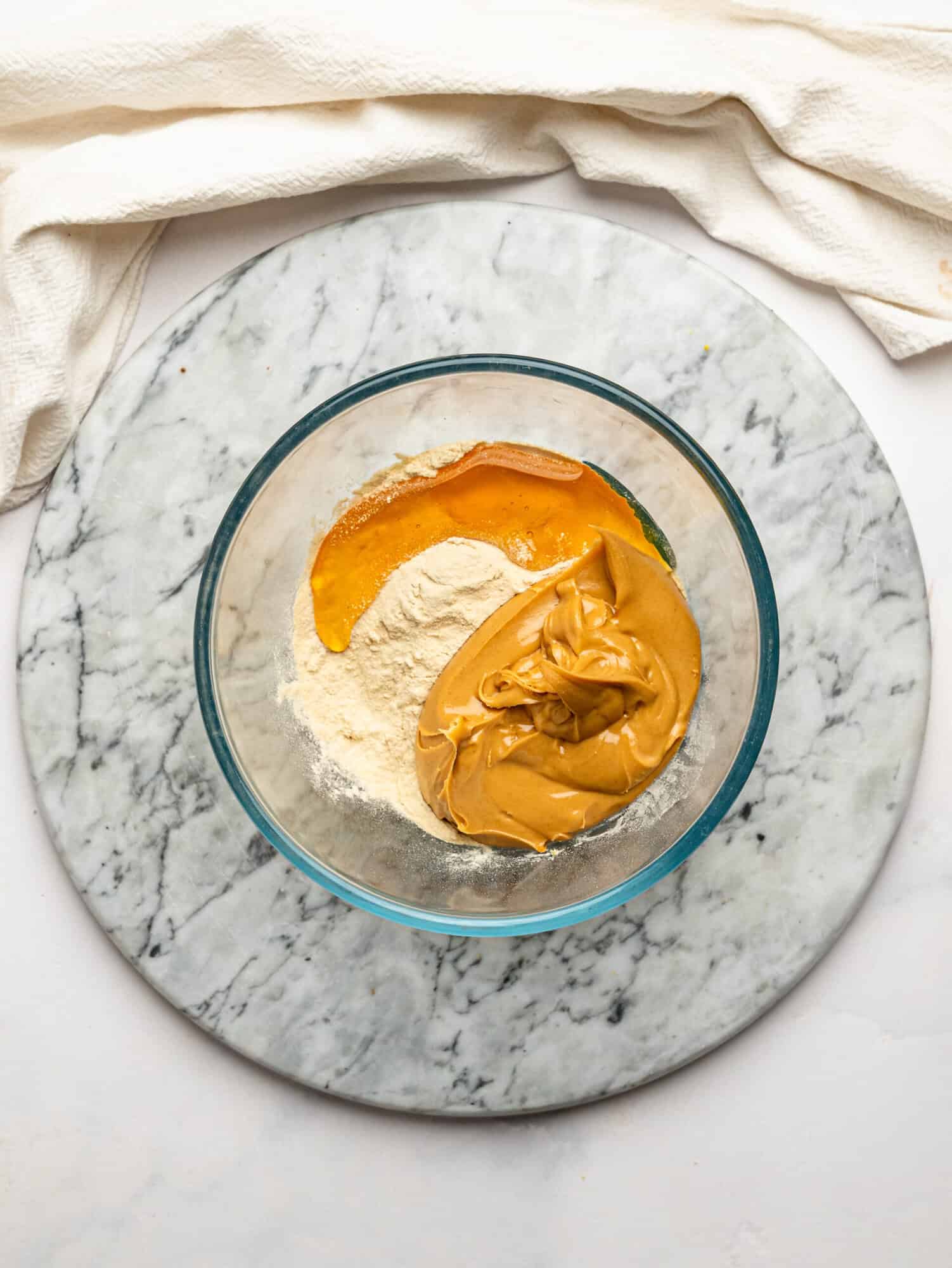 Peanut butter, vanilla protein powder, and liquid sweetener added to a glass mixing bowl before stirring together to make the protein peanut butter cup filling.
