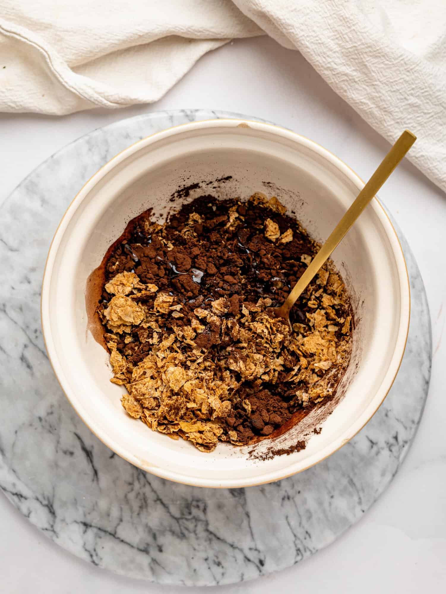 Crushed Weetbix, cocoa powder, and liquid sweetener combined in a mixing bowl to make the chocolate base for Snickers Weetbix Cups.