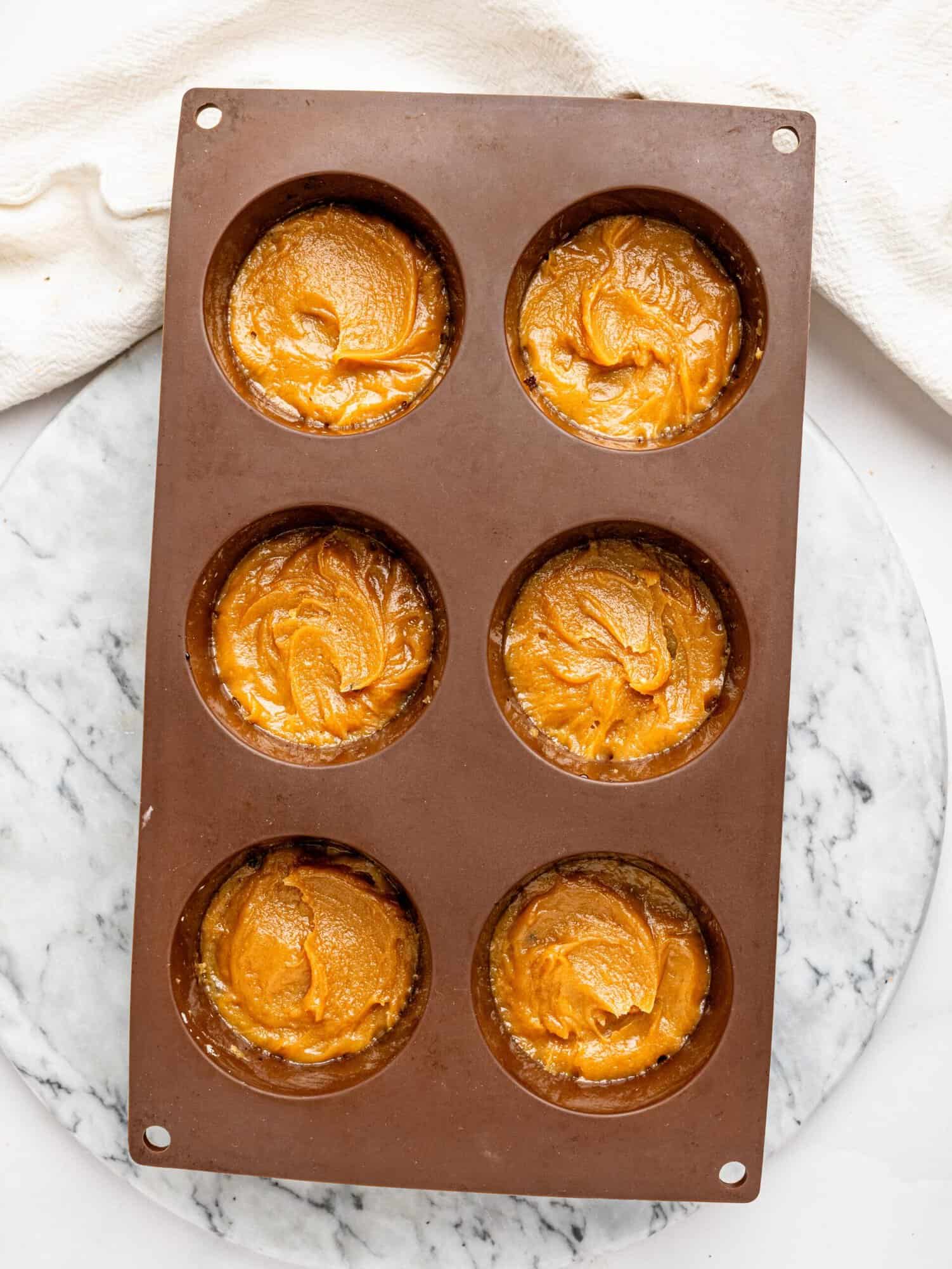 Peanut butter filling evenly distributed into silicone molds for No-Bake Snickers Weetbix Cups before adding toppings.