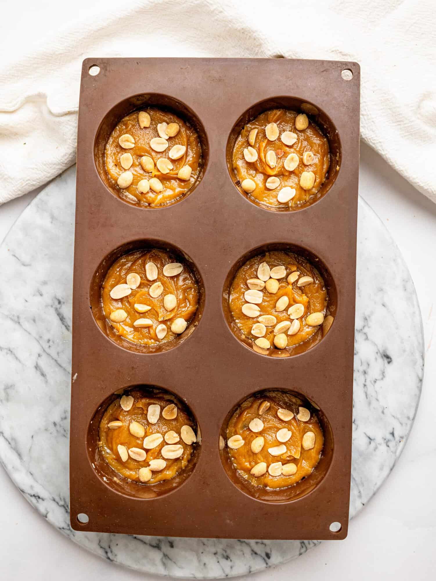 Chopped peanuts sprinkled over the peanut butter layer in silicone molds while preparing Snickers Weetbix Cups.