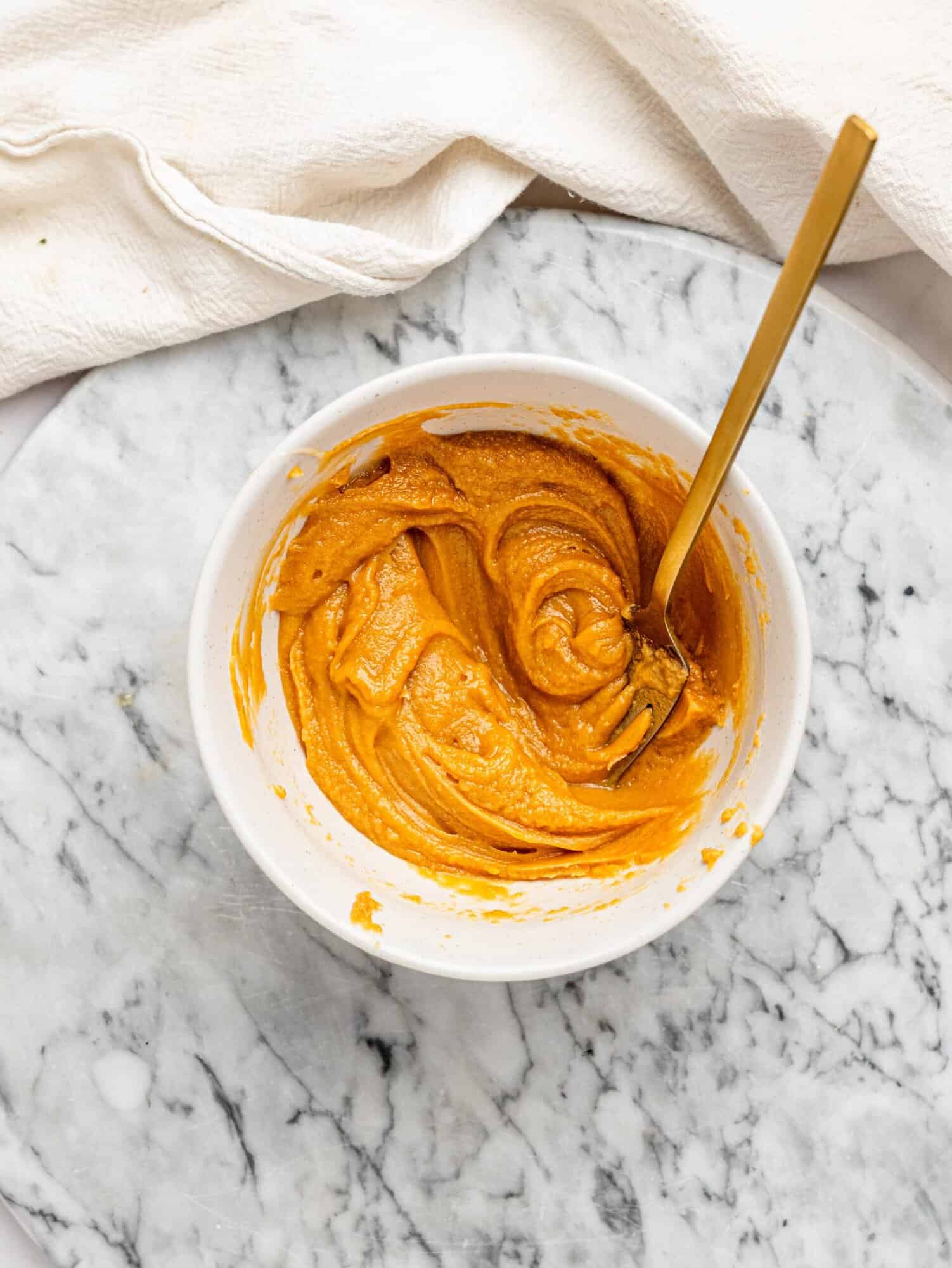 Creamy peanut butter filling mixed in a white bowl with a gold spoon for No-Bake Snickers Weetbix Cups.