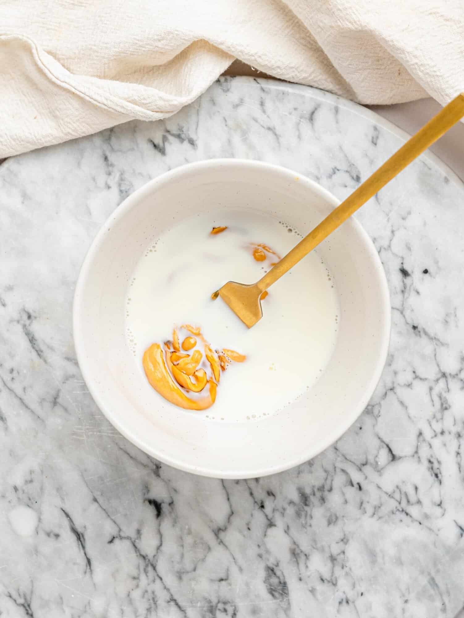 Milk, peanut butter, and honey combined in a bowl to create the creamy filling for Snickers Weetbix Cups.