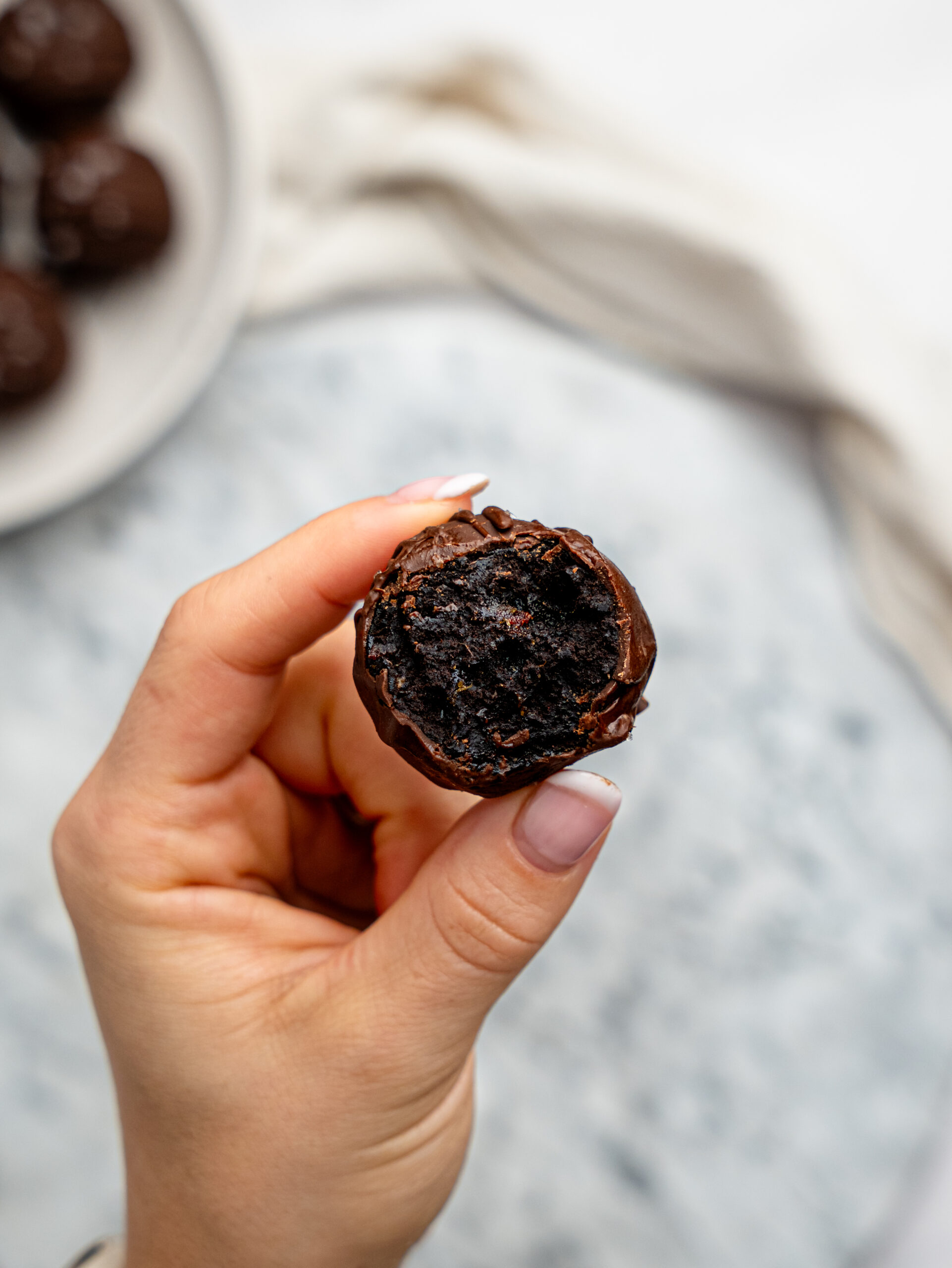 Hand holding a chocolate-coated brownie bite with a bite taken out, showing the rich, fudgy centre.