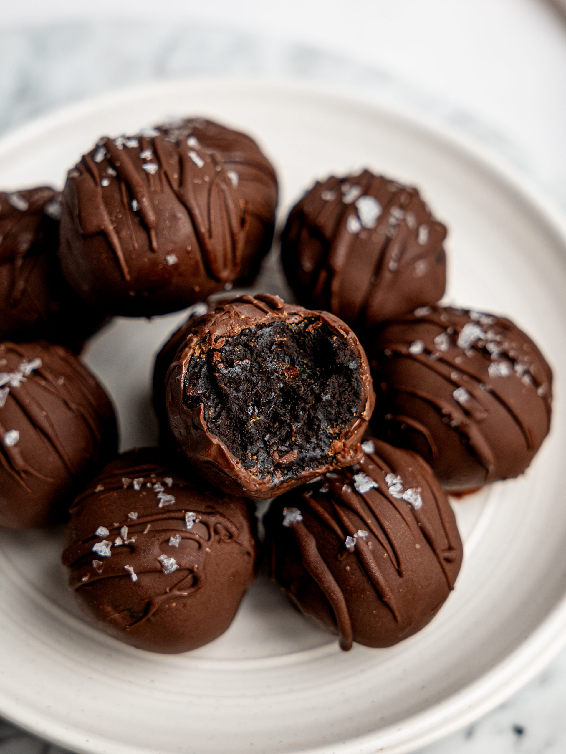 Close-up of fudgy no-bake brownie bites coated in dark chocolate and finished with flaky sea salt.