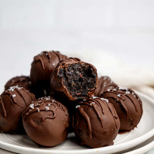 Chocolate-coated brownie bites stacked on a white plate with one bite showing the soft brownie-like centre.
