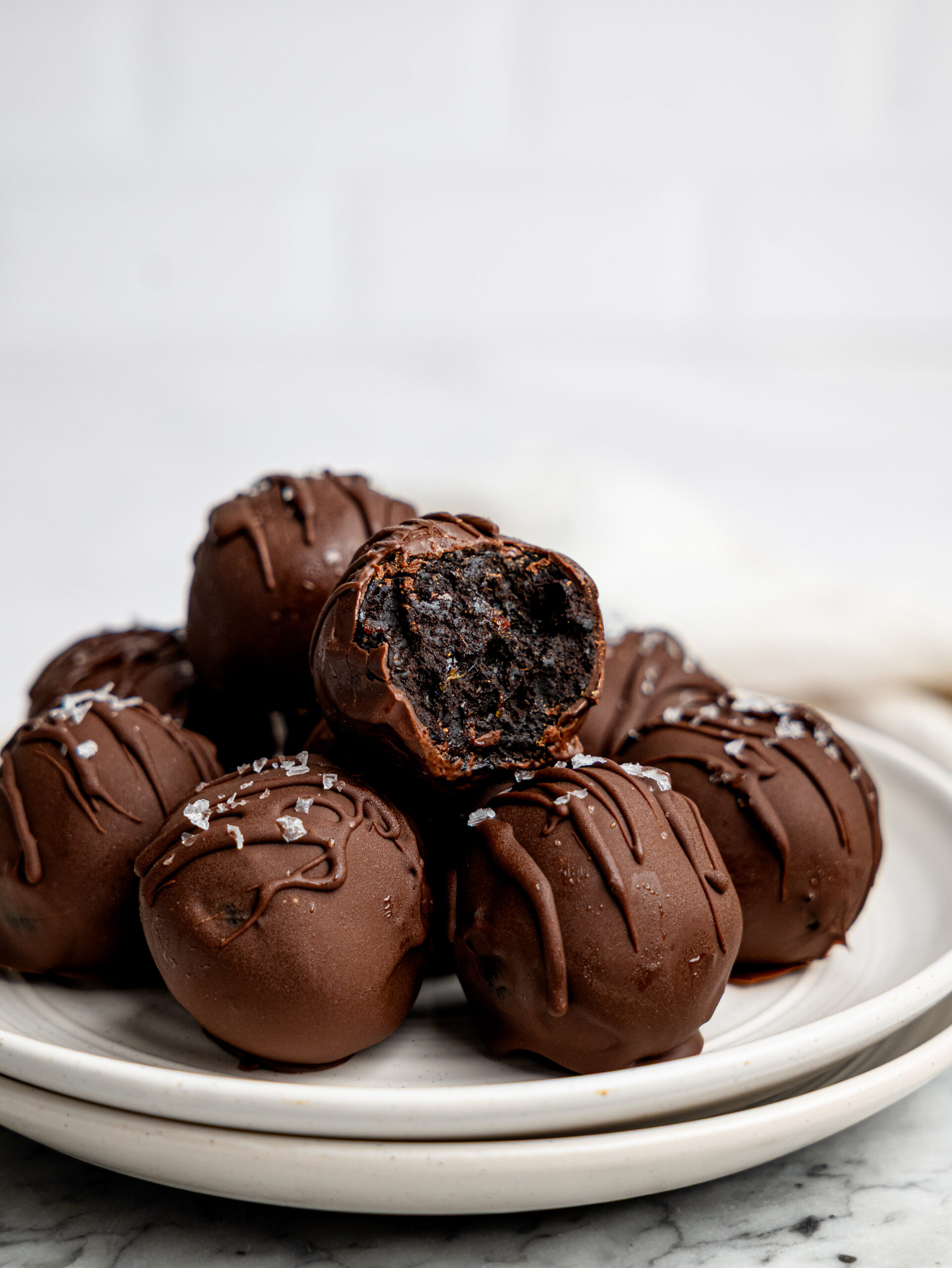 Chocolate-coated brownie bites stacked on a white plate with one bite showing the soft brownie-like centre.