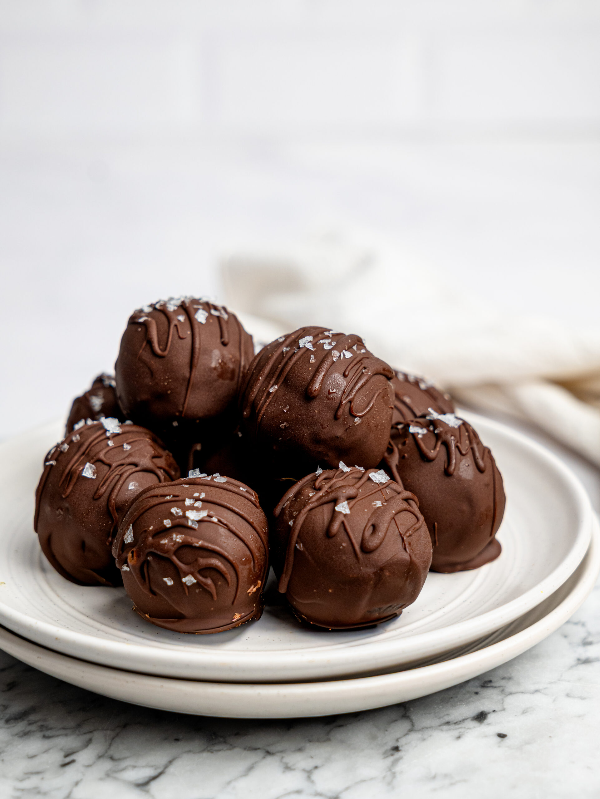 Chocolate brownie bites arranged on a white plate, coated in dark chocolate with a drizzle and sea salt topping.