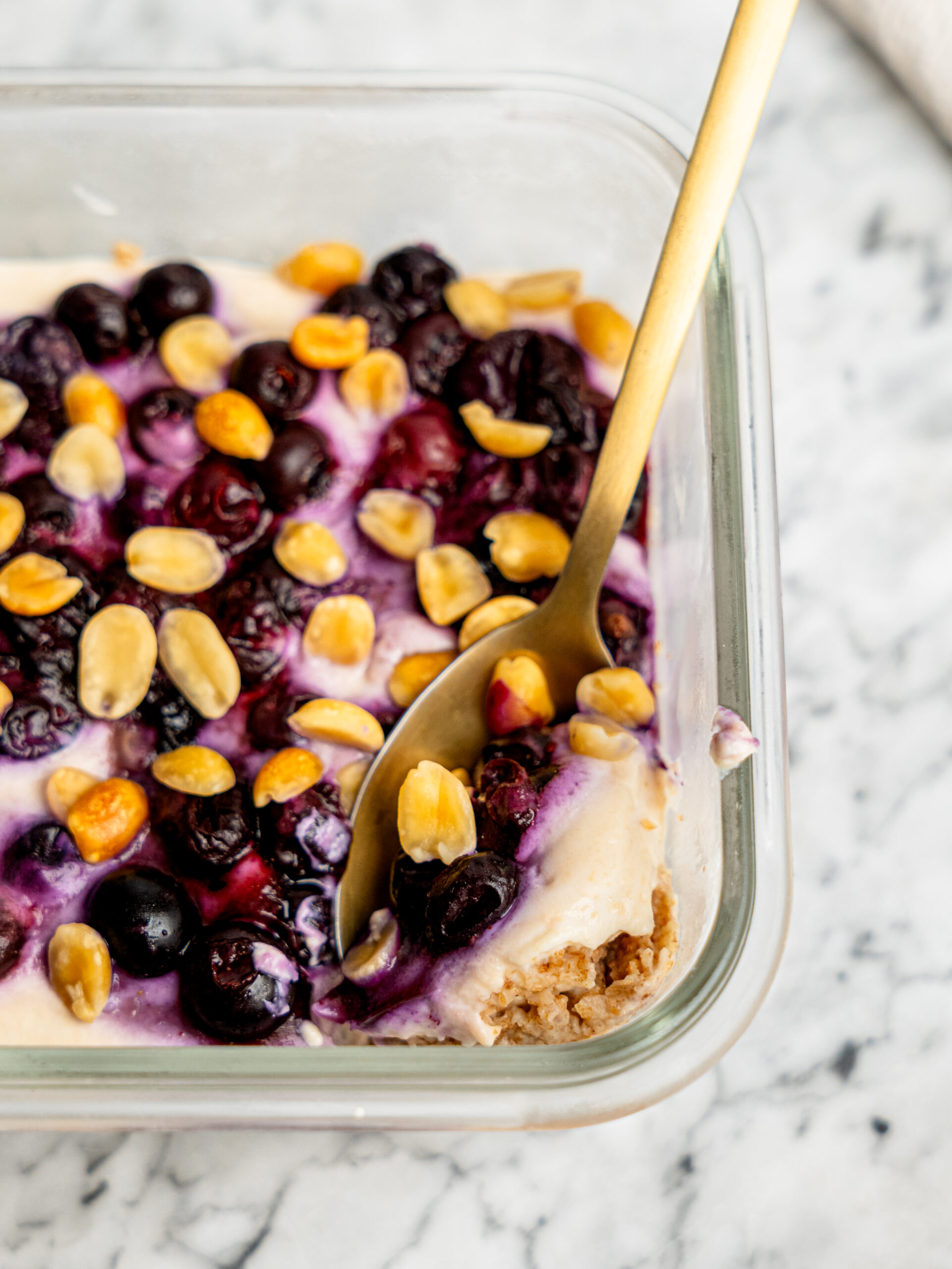 Golden spoon scooping a creamy bite of PB&J Overnight Weetbix topped with juicy berries and crunchy peanuts.